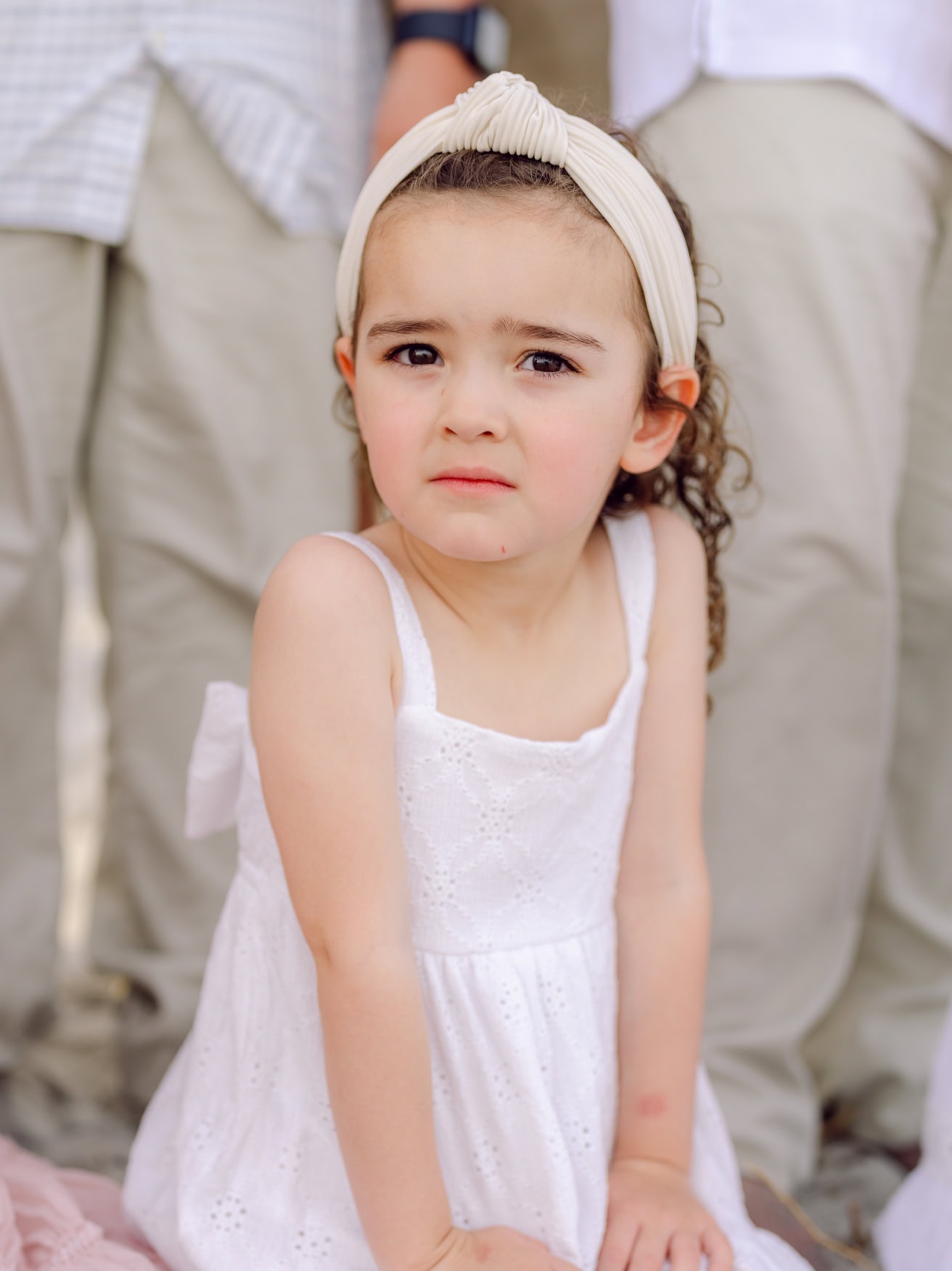 Young girl in a white dress during a family portrait session at Wild Dunes Resort in Isle of Palms near Charleston, South Carolina. Candid child portrait on the beach with soft evening light and coastal dunes in the background.