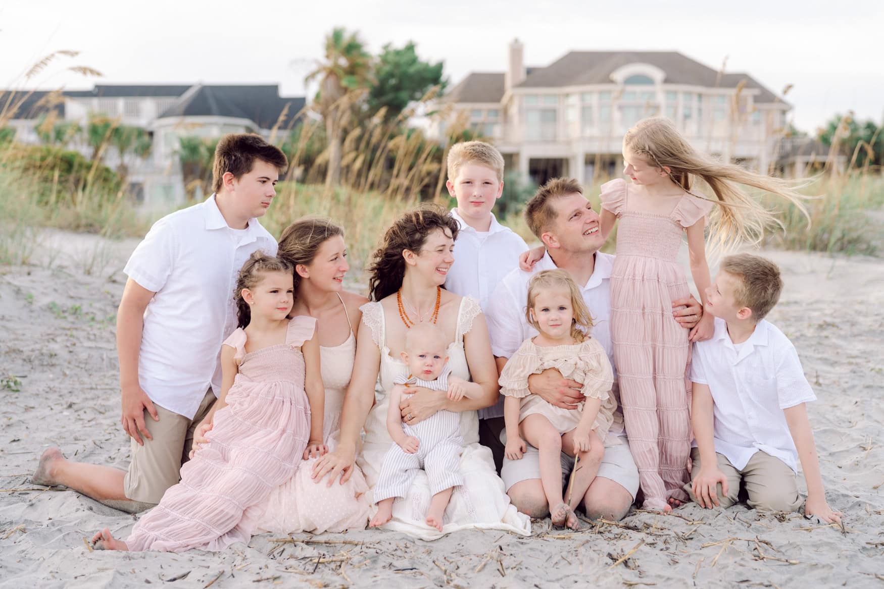 Family of ten enjoying a candid beach portrait at Wild Dunes Resort in Isle of Palms near Charleston, South Carolina. Parents and children sharing natural moments together during a sunset family photography session with sea oats and coastal homes in the background.