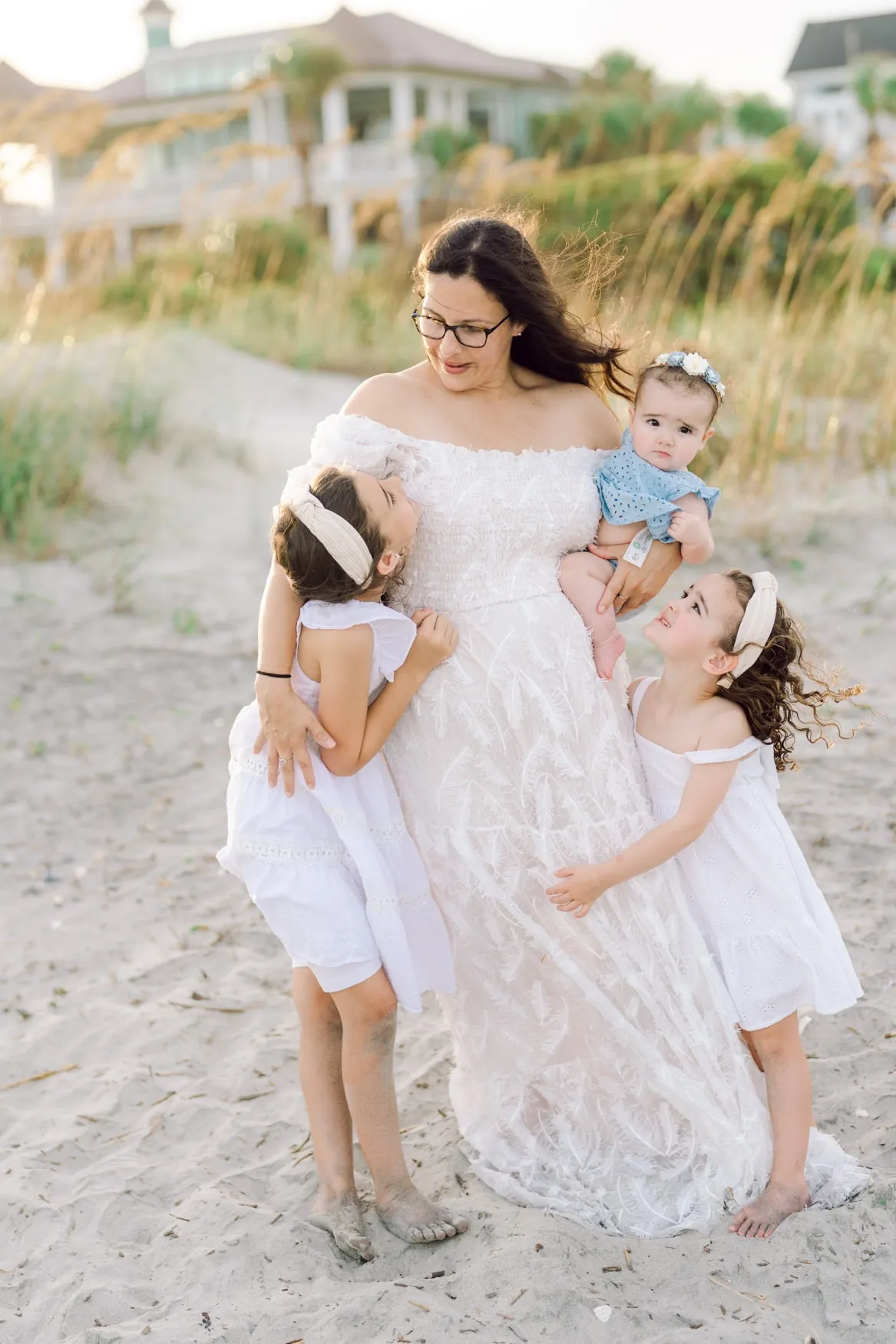 Mother holding her baby while two daughters hug her during a golden hour family beach photography session at Isle of Palms near Wild Dunes Resort in Charleston, South Carolina.