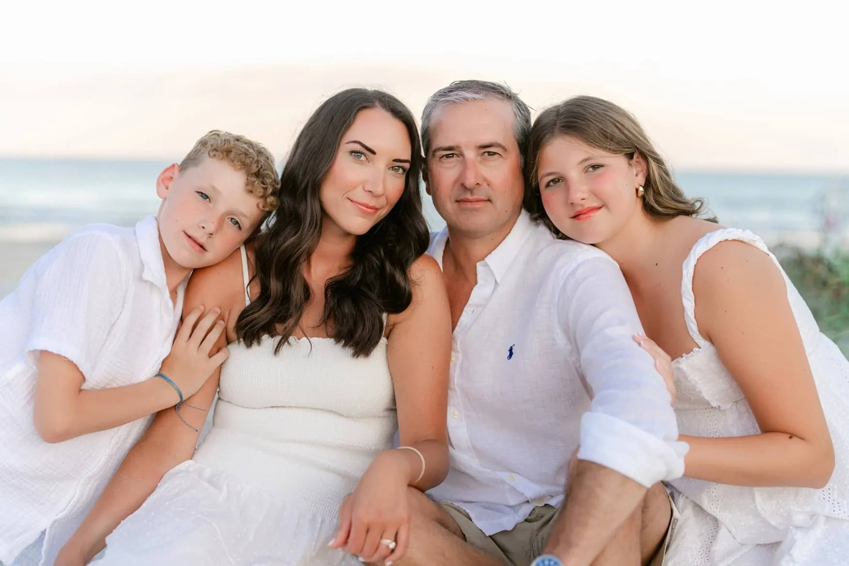 Family with hair and fabric moving naturally in the wind during a beach family photo session in Myrtle Beach, South Carolina.
