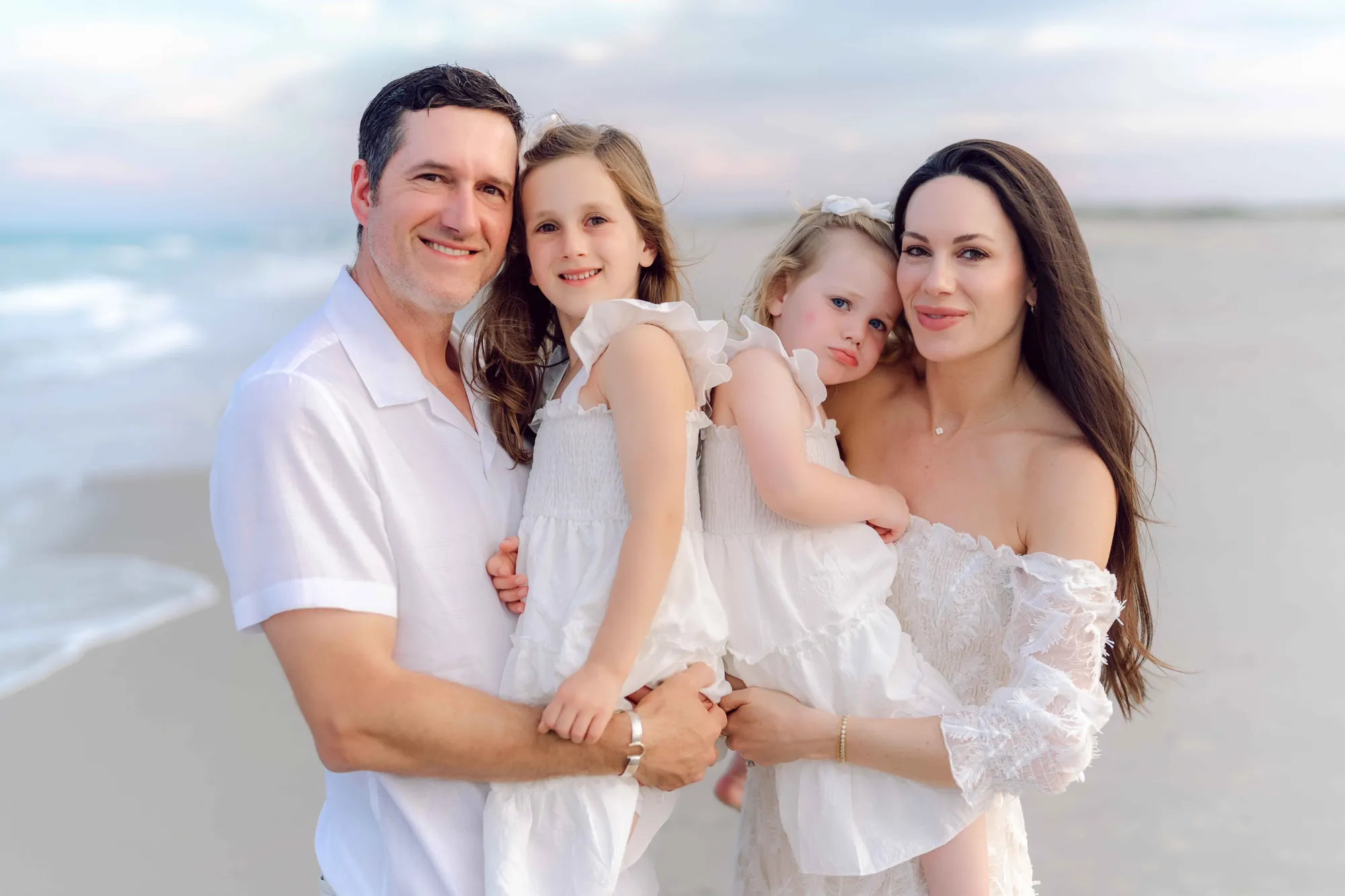 Parents standing together while their daughters play on the beach in Pawleys Island.