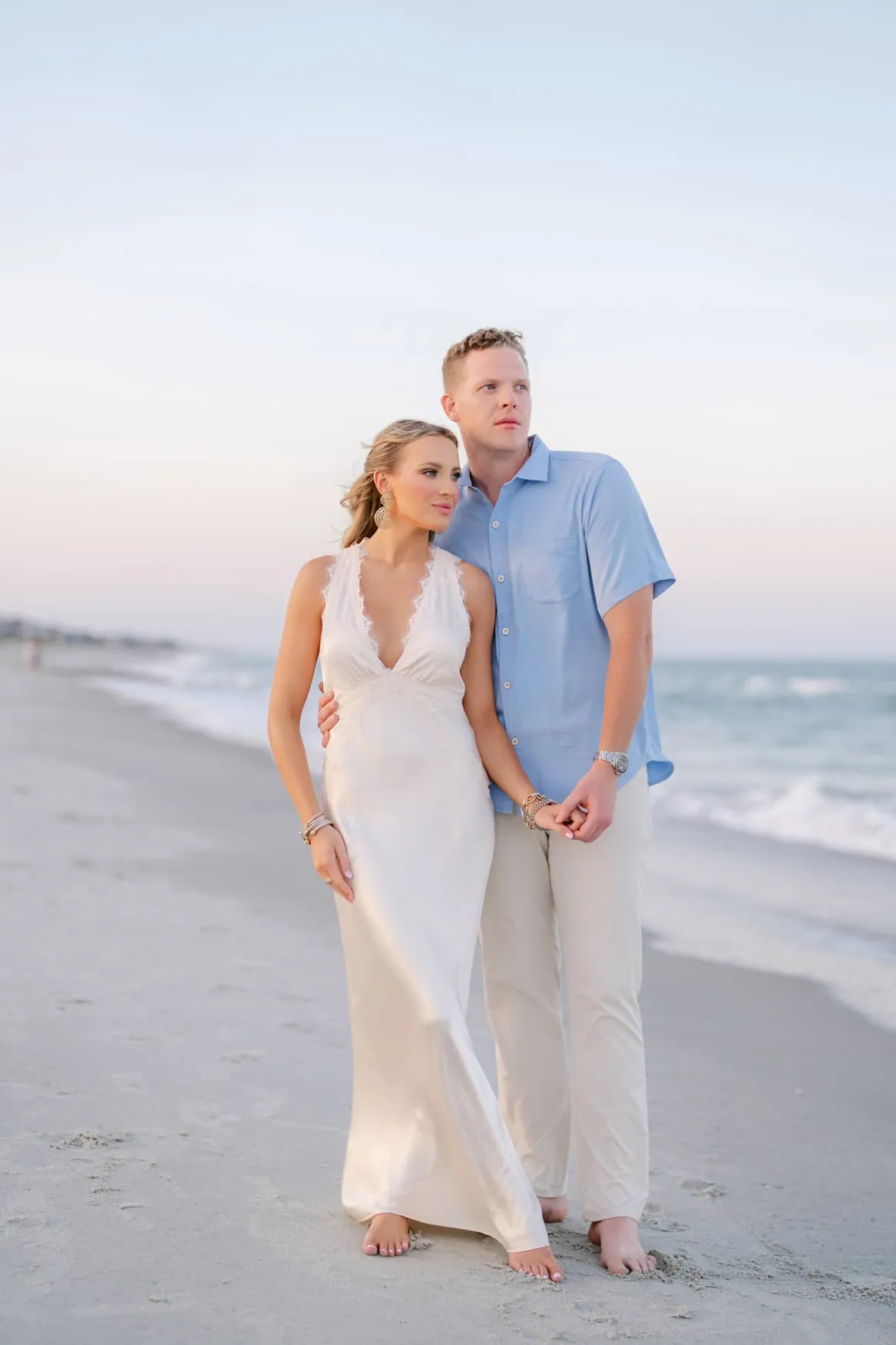 Couple barefoot on the beach in a flowing ivory dress and light blue shirt