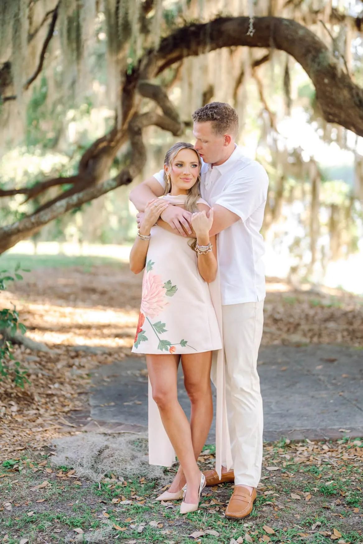 Couple in a floral mini dress and relaxed white shirt beneath Spanish moss in Charleston