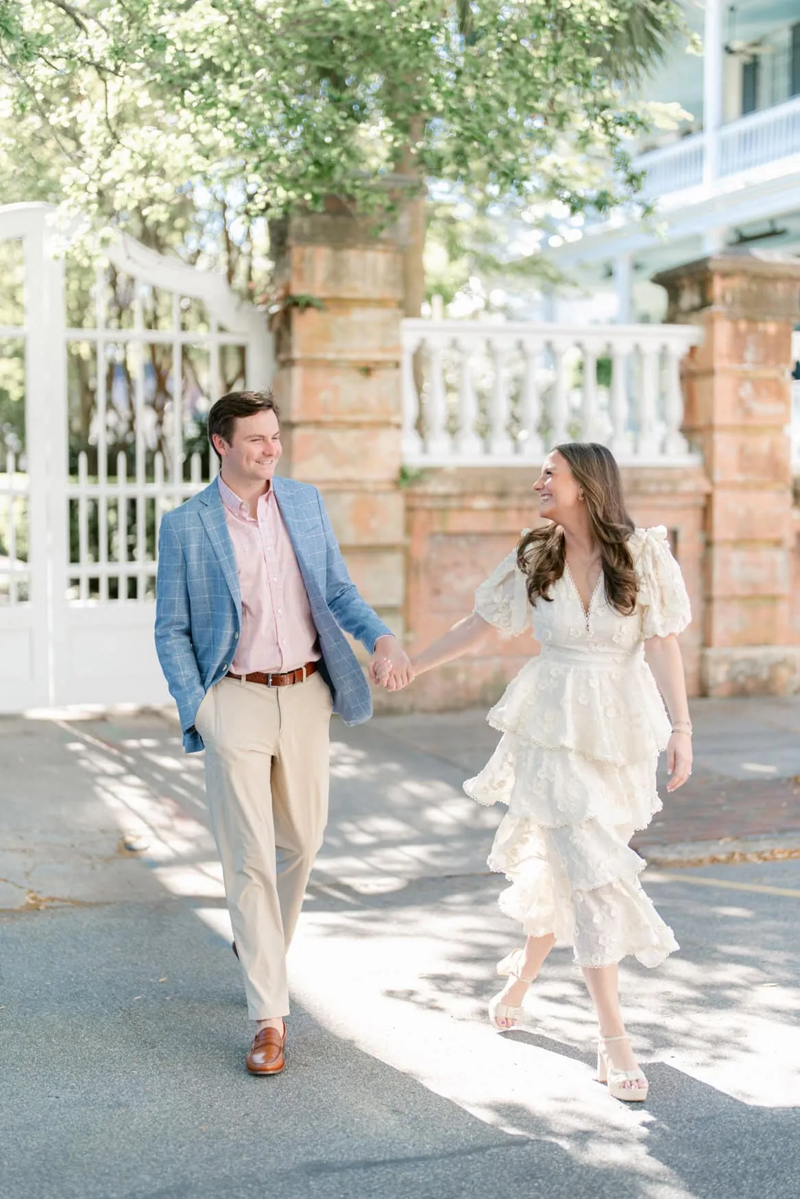 Couple in a tiered ivory dress and blue blazer walking through downtown Charleston