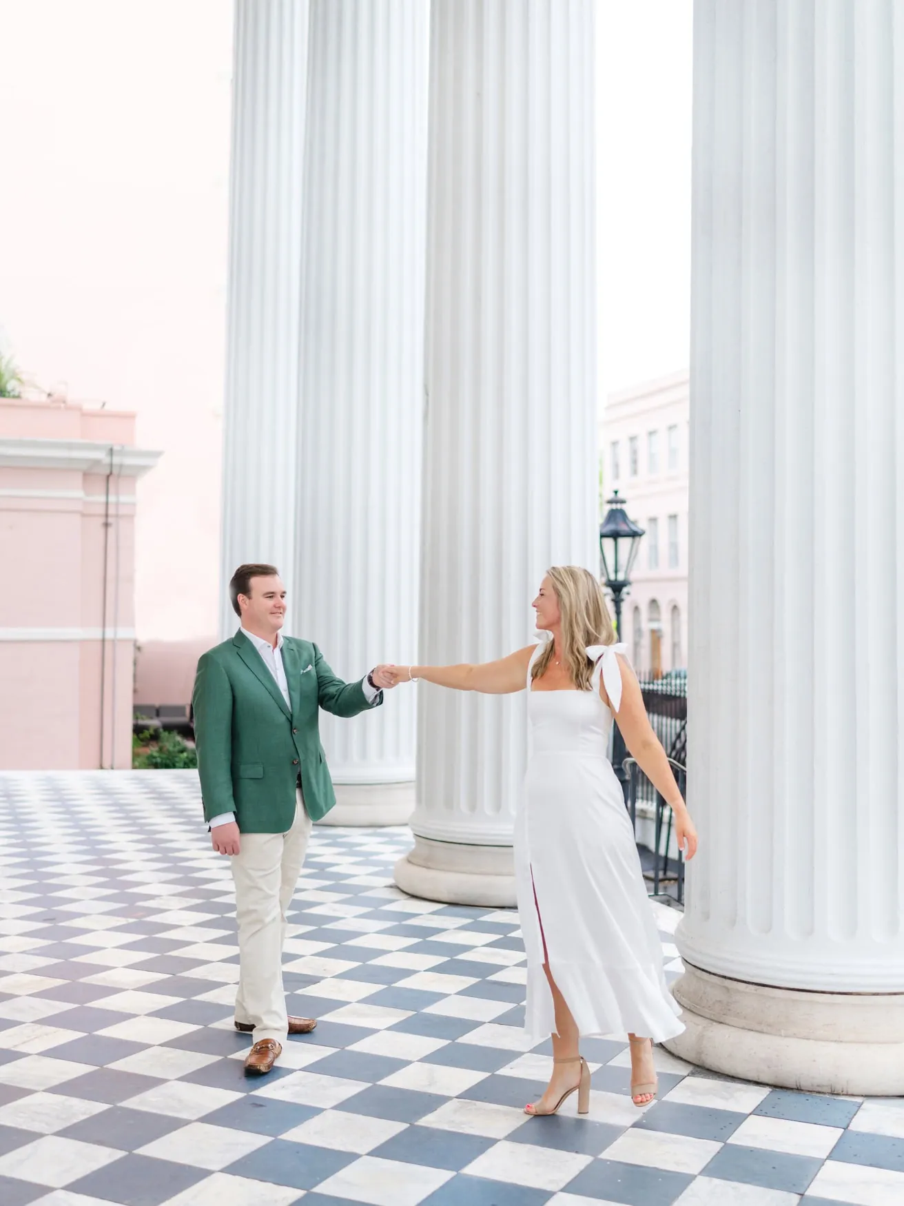 Couple in a white midi dress and green blazer among Charleston columns and checkerboard flooring