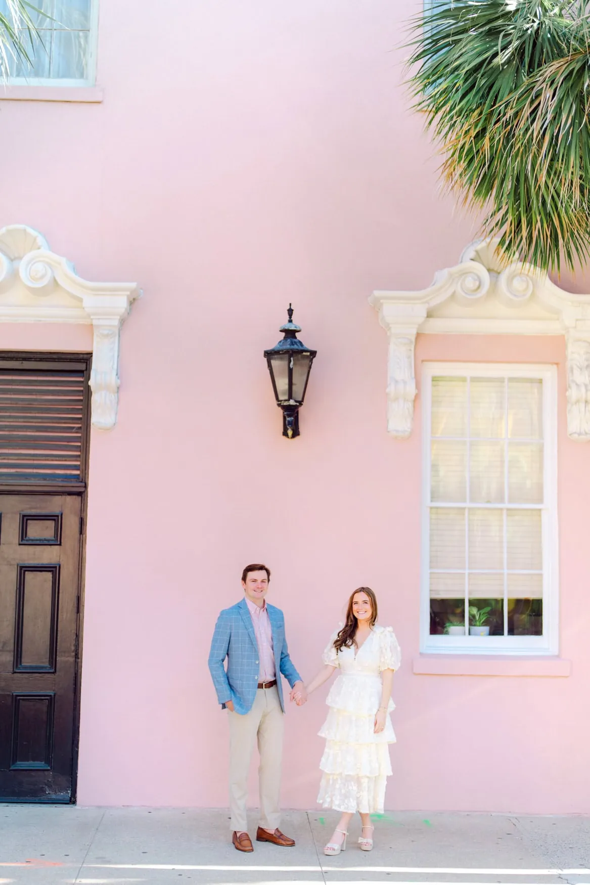 Couple in an ivory tiered dress and blue blazer in front of a pink Charleston facade