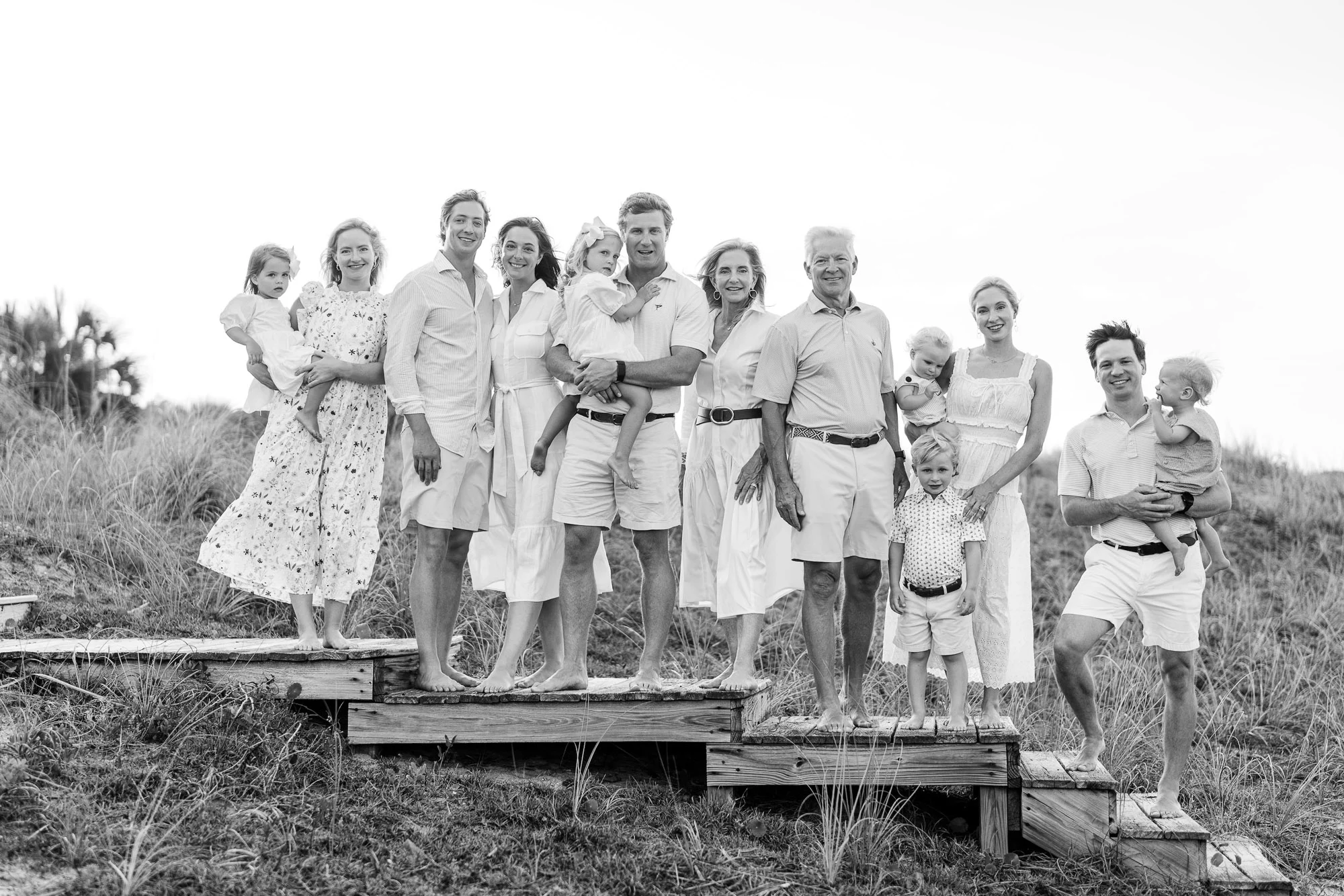 Extended family of three generations standing together on a wooden dune walkway in black and white, Myrtle Beach family photography by Pasha Belman