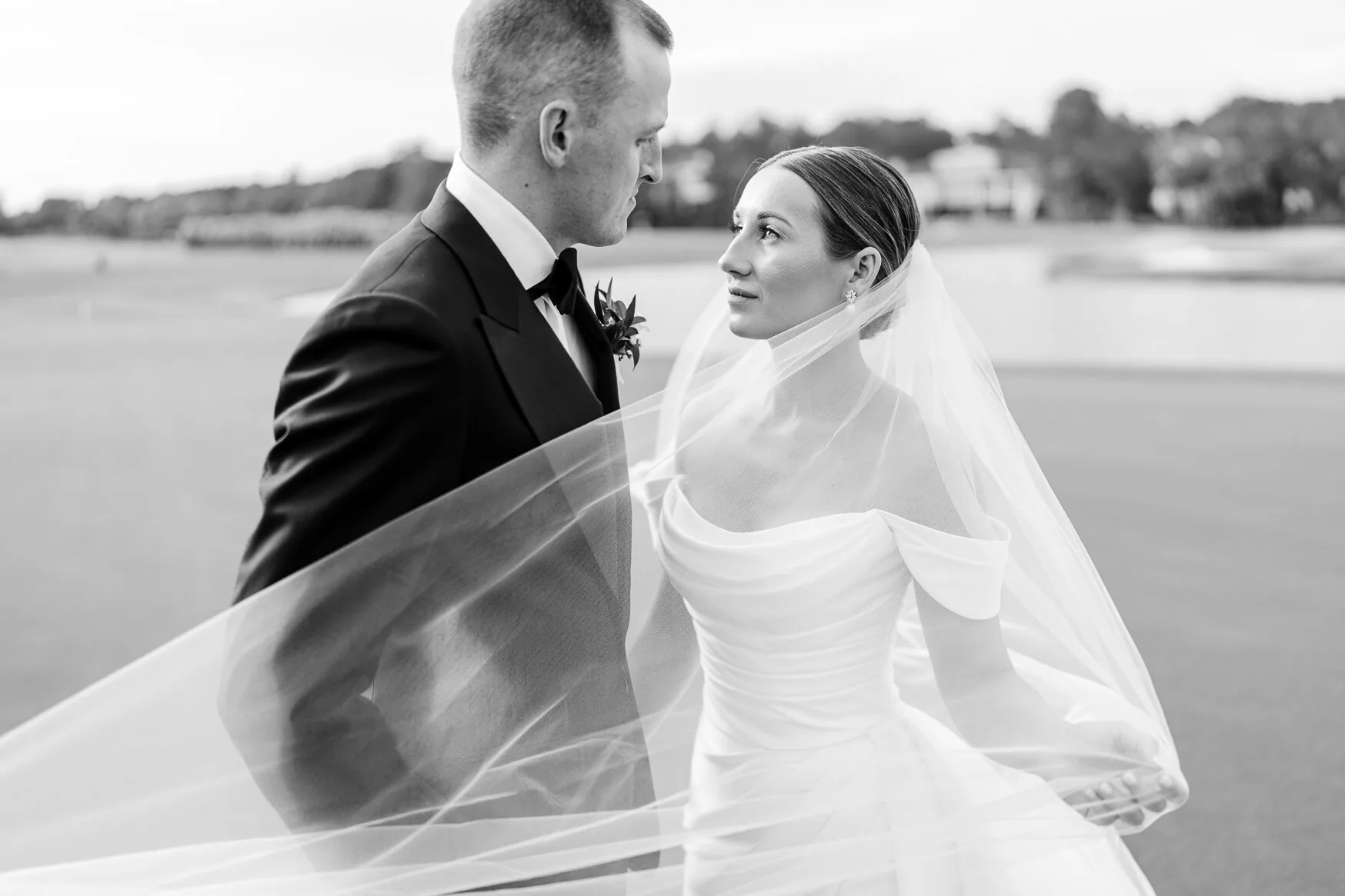 Black and white portrait of a bride and groom with her veil blowing in the wind on a golf course near Pawleys Island