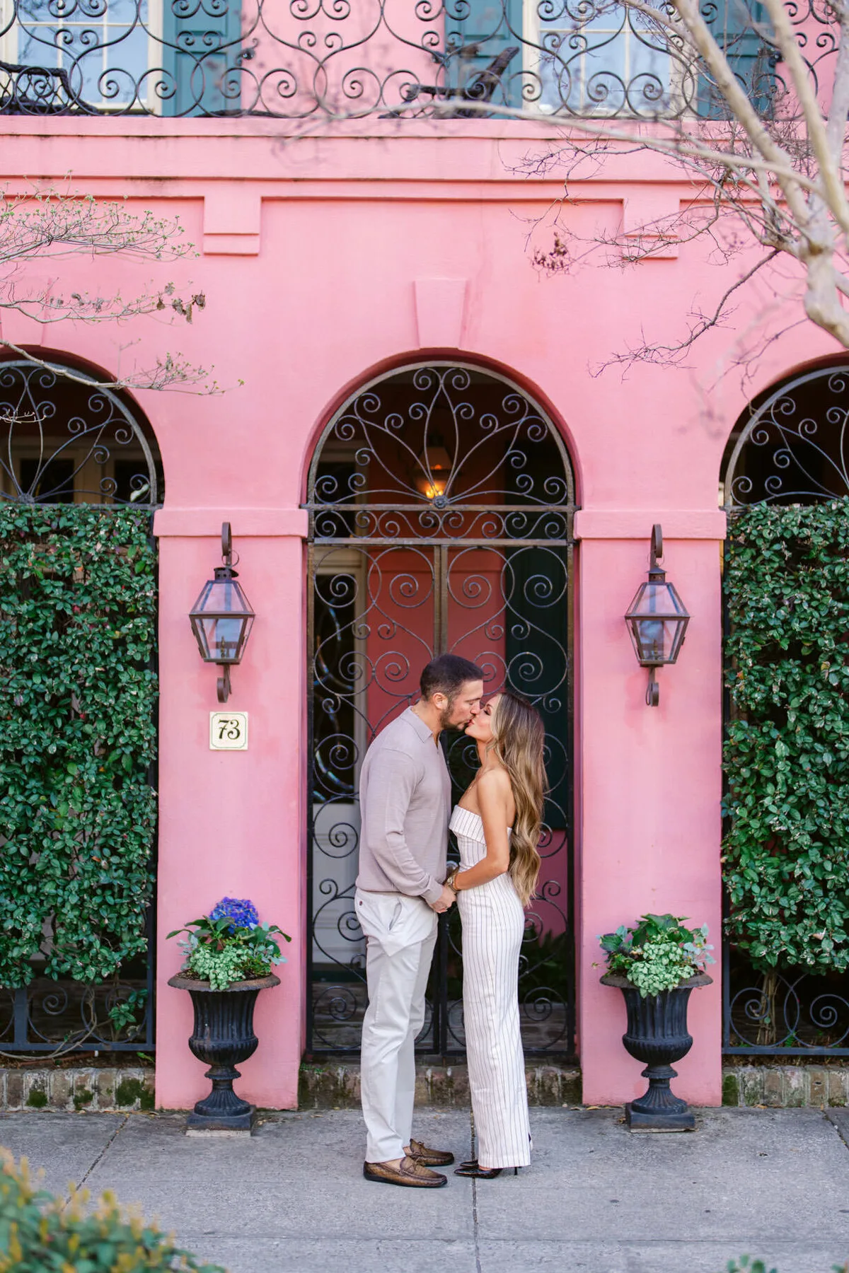 Engaged couple kissing at a pink doorway on Rainbow Row in Charleston SC