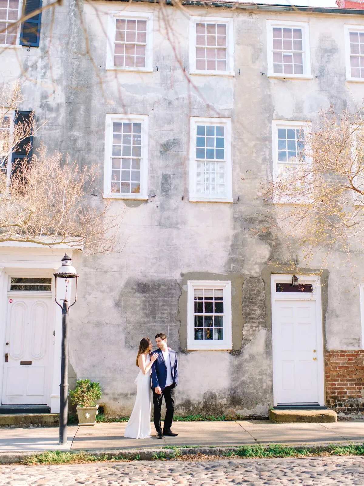 Engaged couple standing by an old building with a street lamp in Charleston SC