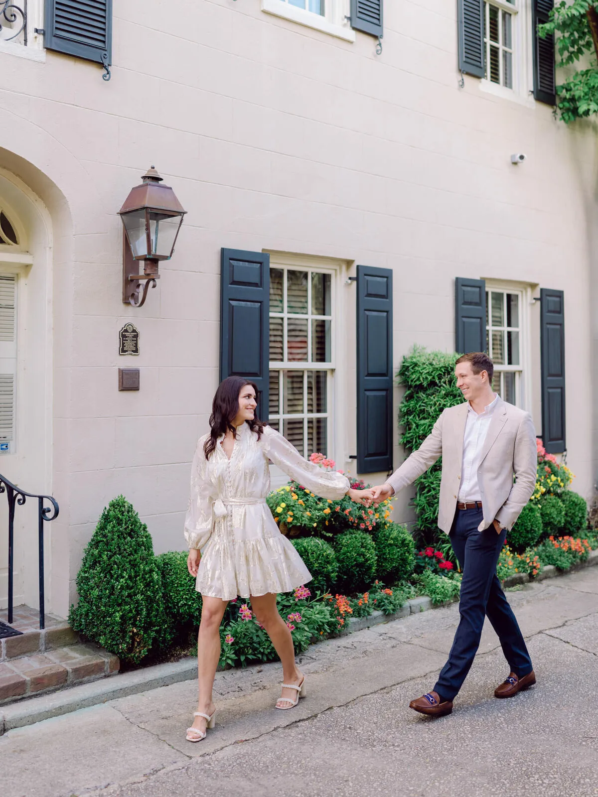 Engaged couple walking and laughing past a Charleston townhouse