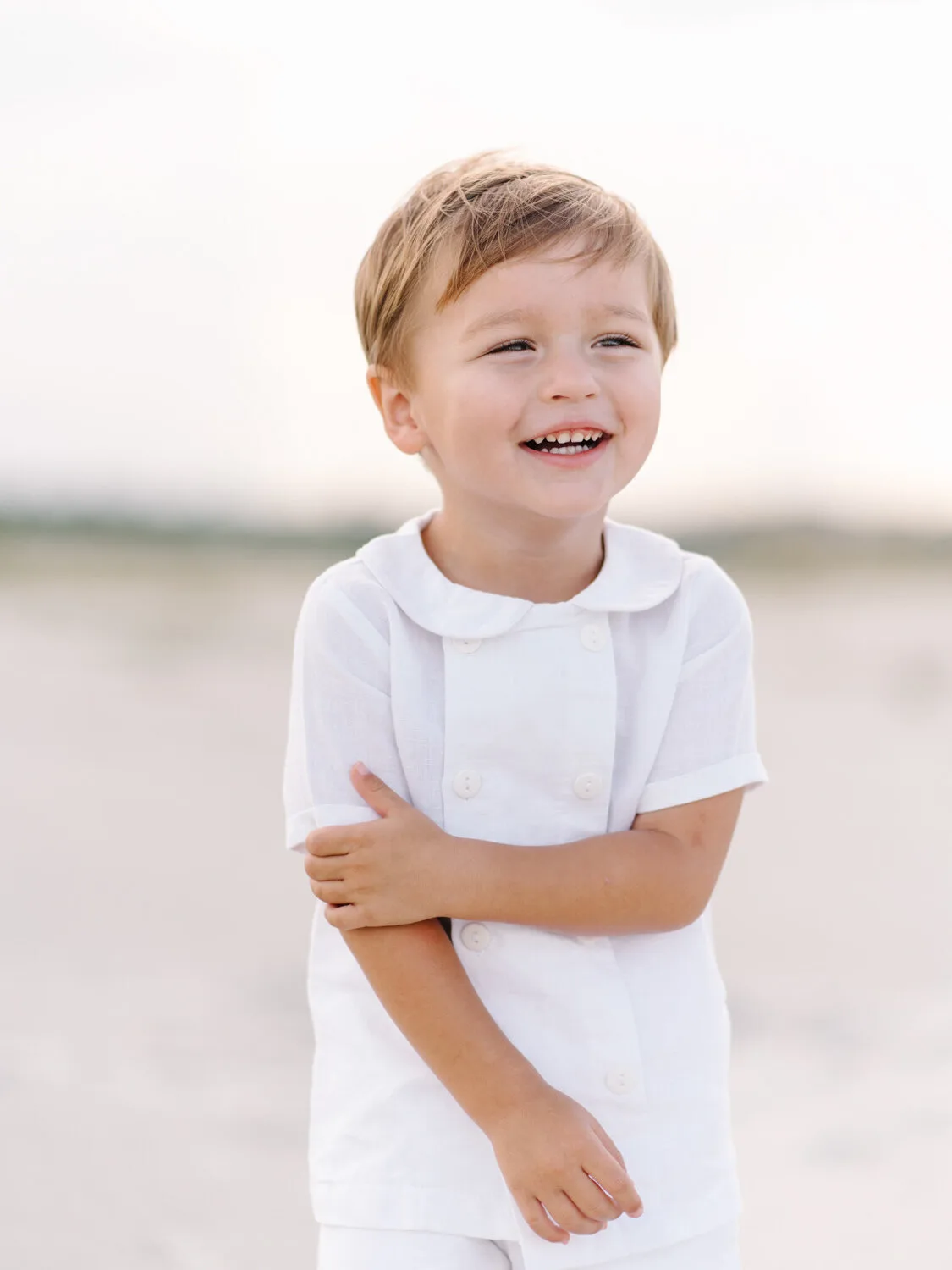Little boy smiling in a white shirt on the beach near Charleston SC