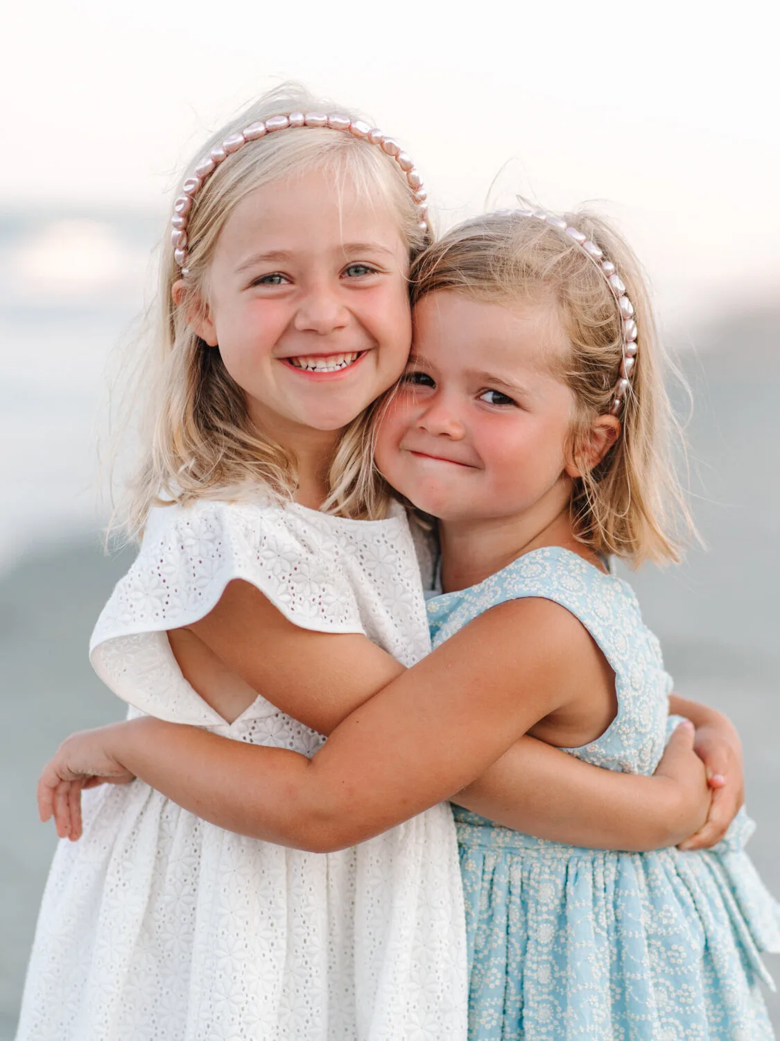 Two sisters hugging in pearl headbands on the beach near Charleston SC