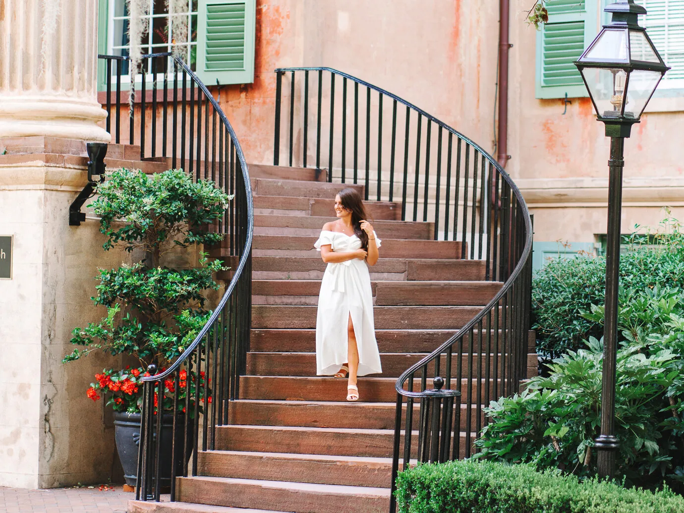 College senior in a white dress walking up a curved brick staircase with a gas lantern in historic Charleston