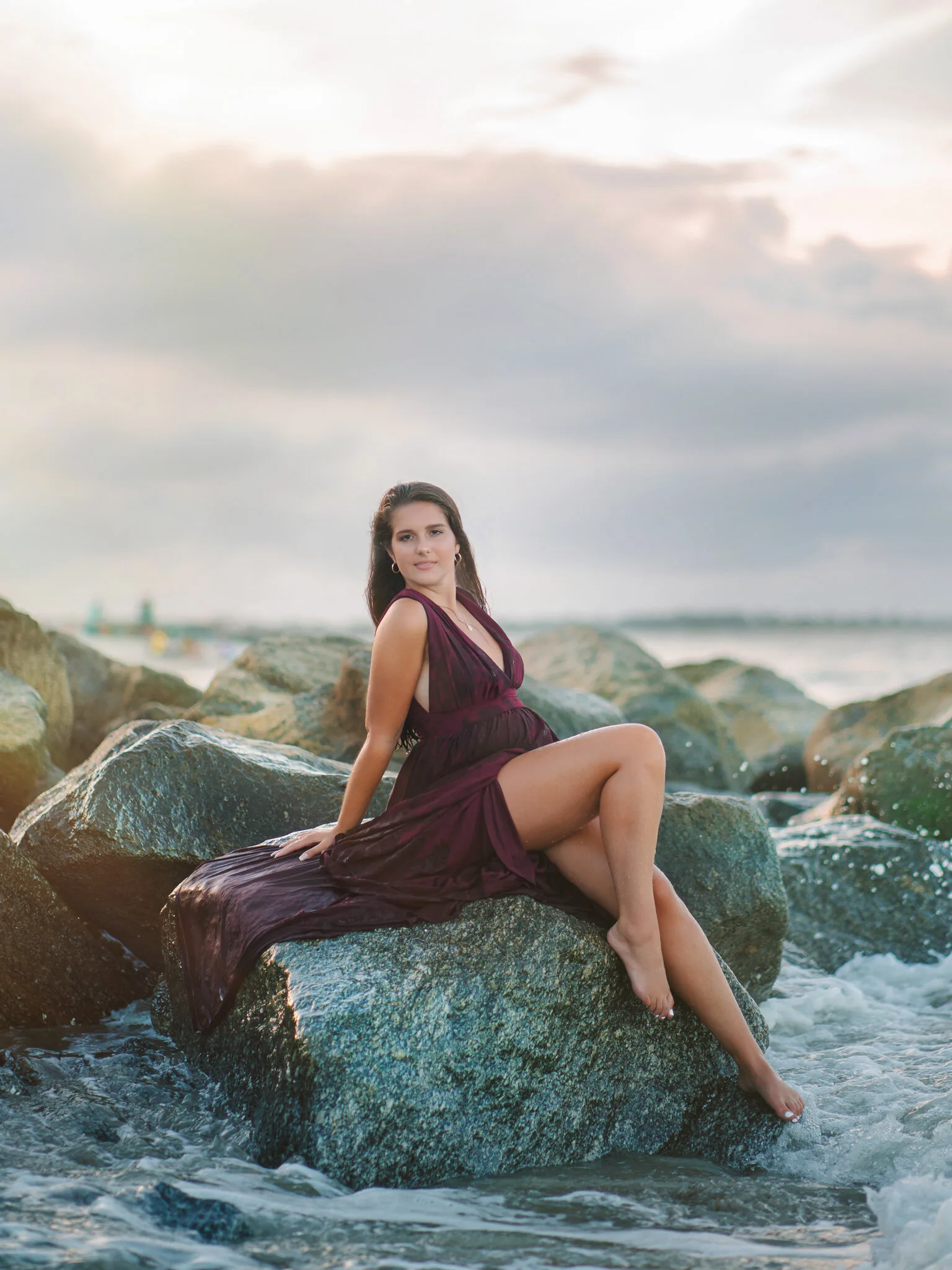 Charleston high school senior in a plum wrap dress sitting on coastal rocks at sunset by Charleston senior photographer Pasha Belman