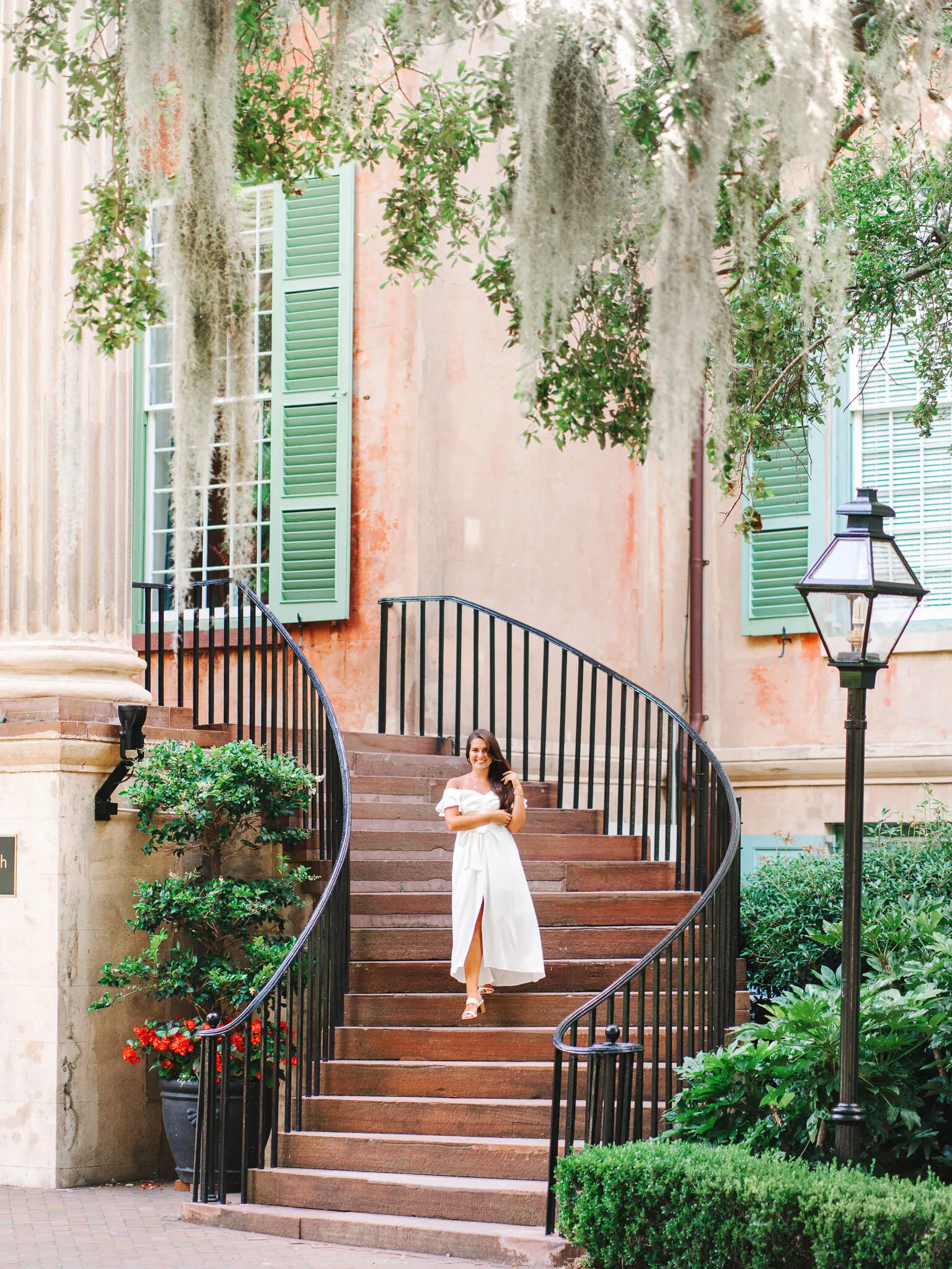 Senior girl in a white dress on a curved brick staircase with a gas lantern and Spanish moss in Charleston