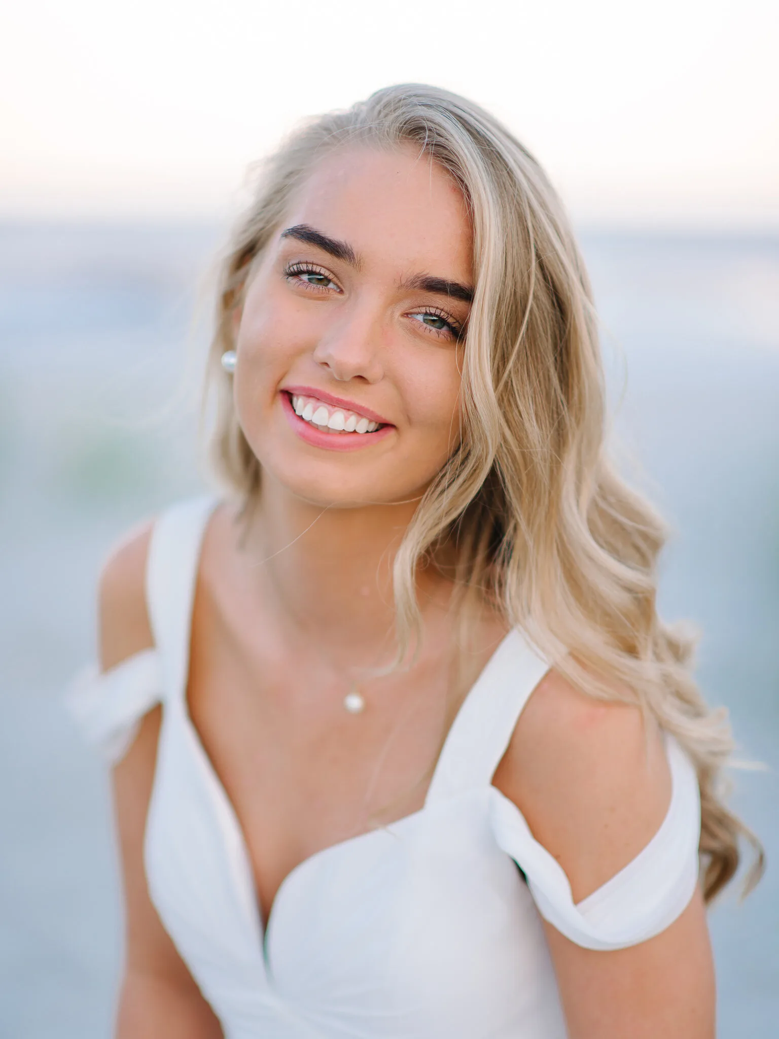 Smiling blonde senior girl in a white off-the-shoulder top on the beach near Charleston