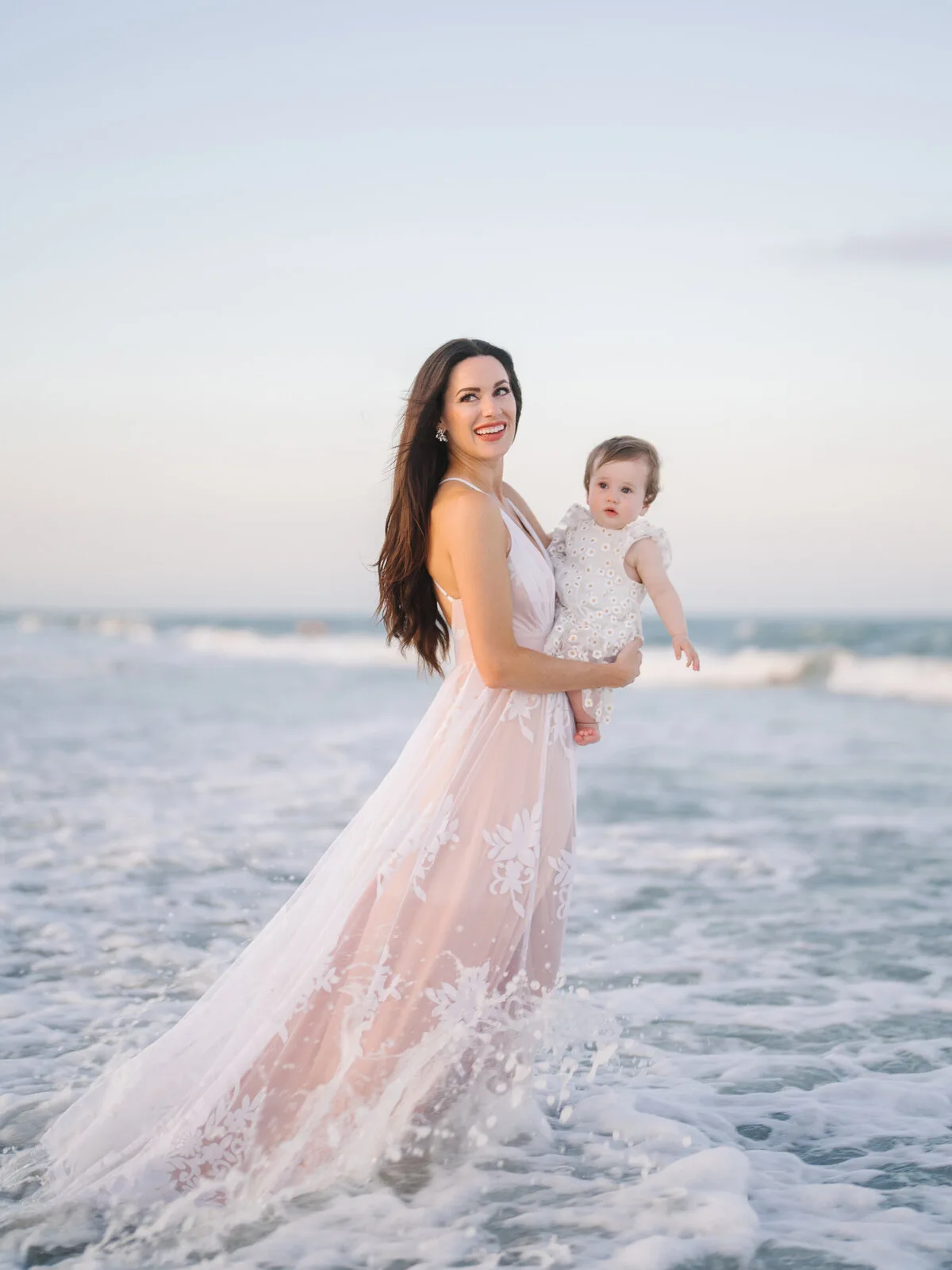 Mother in a pink gown holding her toddler in the surf in Garden City Beach SC
