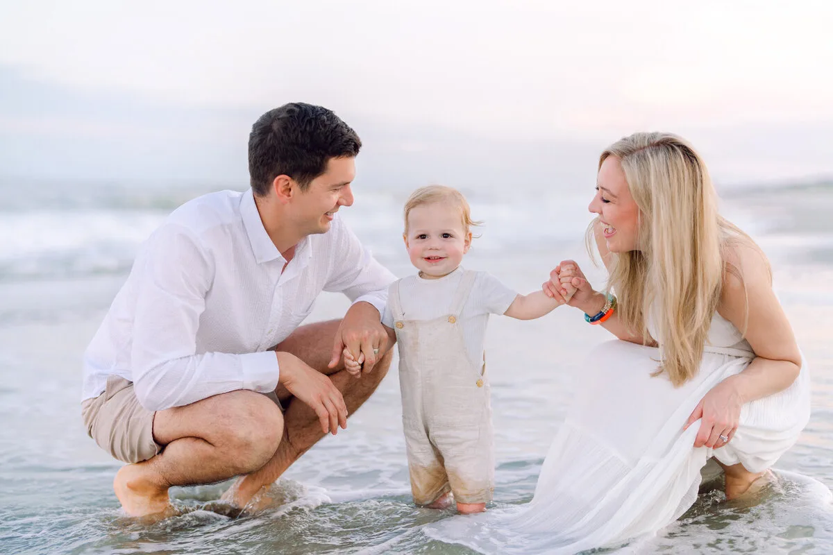 Parents crouching with their toddler in the shallow surf in Garden City Beach SC