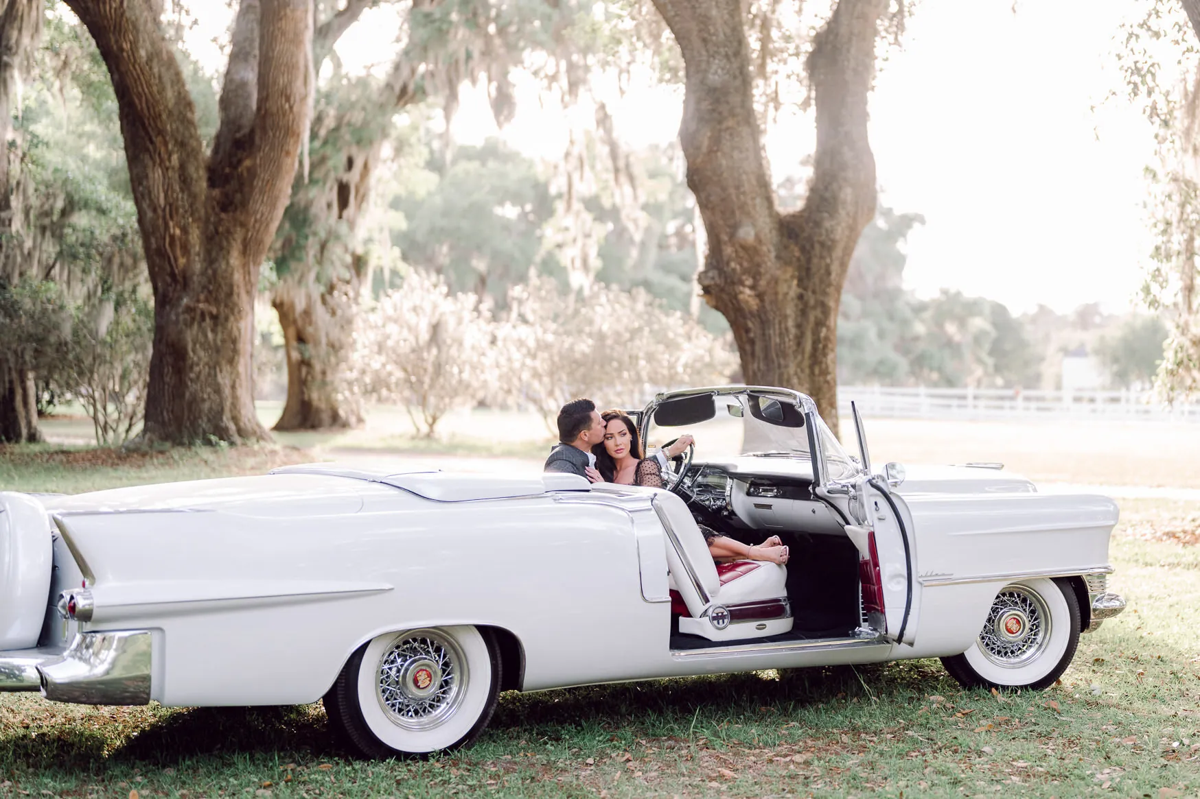 Vintage white convertible parked under live oaks with an engaged couple sitting inside, photographed on the Grand Strand