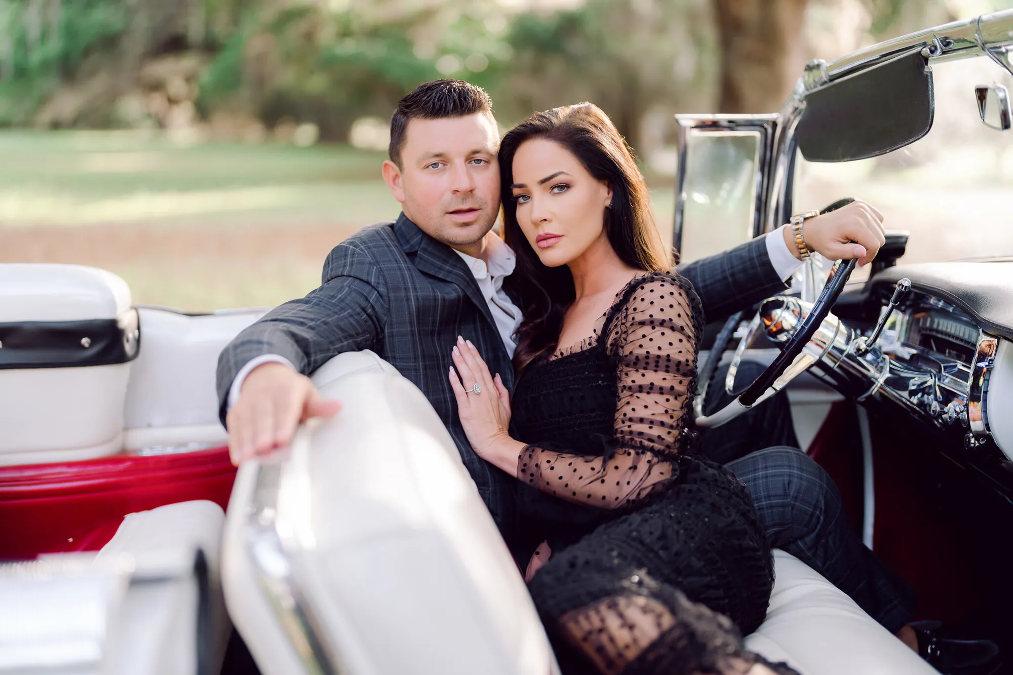 Engaged couple in dark outfits posing in the front seat of a vintage convertible for an editorial engagement session near Myrtle Beach