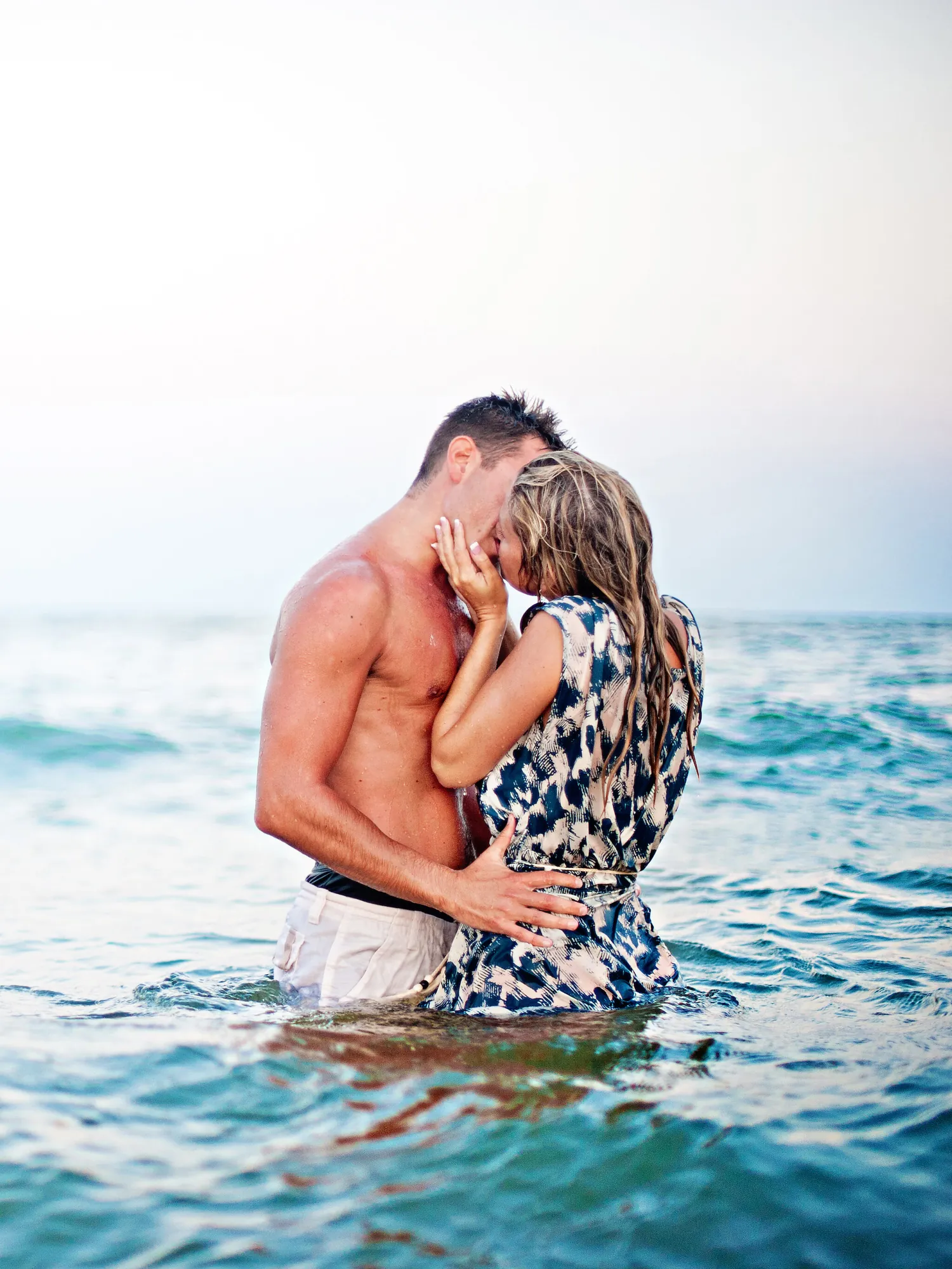 Engaged couple kissing waist-deep in turquoise ocean water during a Myrtle Beach engagement session