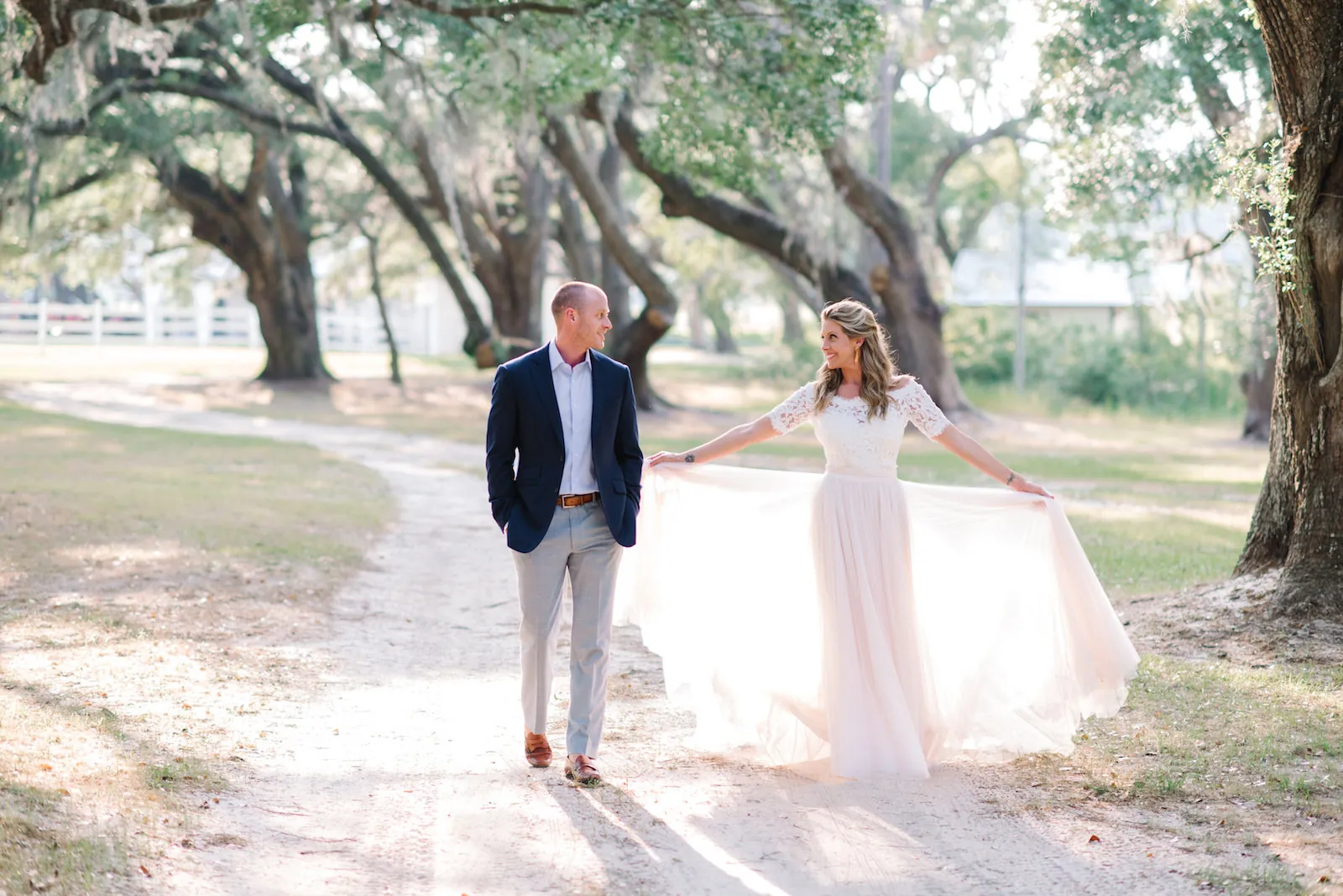 Engaged couple walking under live oaks at Mansfield Plantation, her tulle skirt spread in the breeze