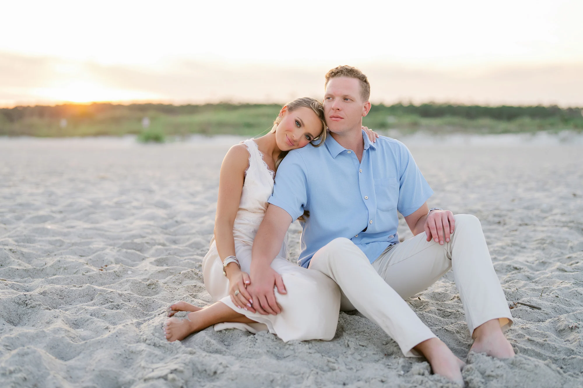 Engaged couple sitting together on the sand at sunset as she rests her head on his shoulder, Myrtle Beach engagement photography by Pasha Belman