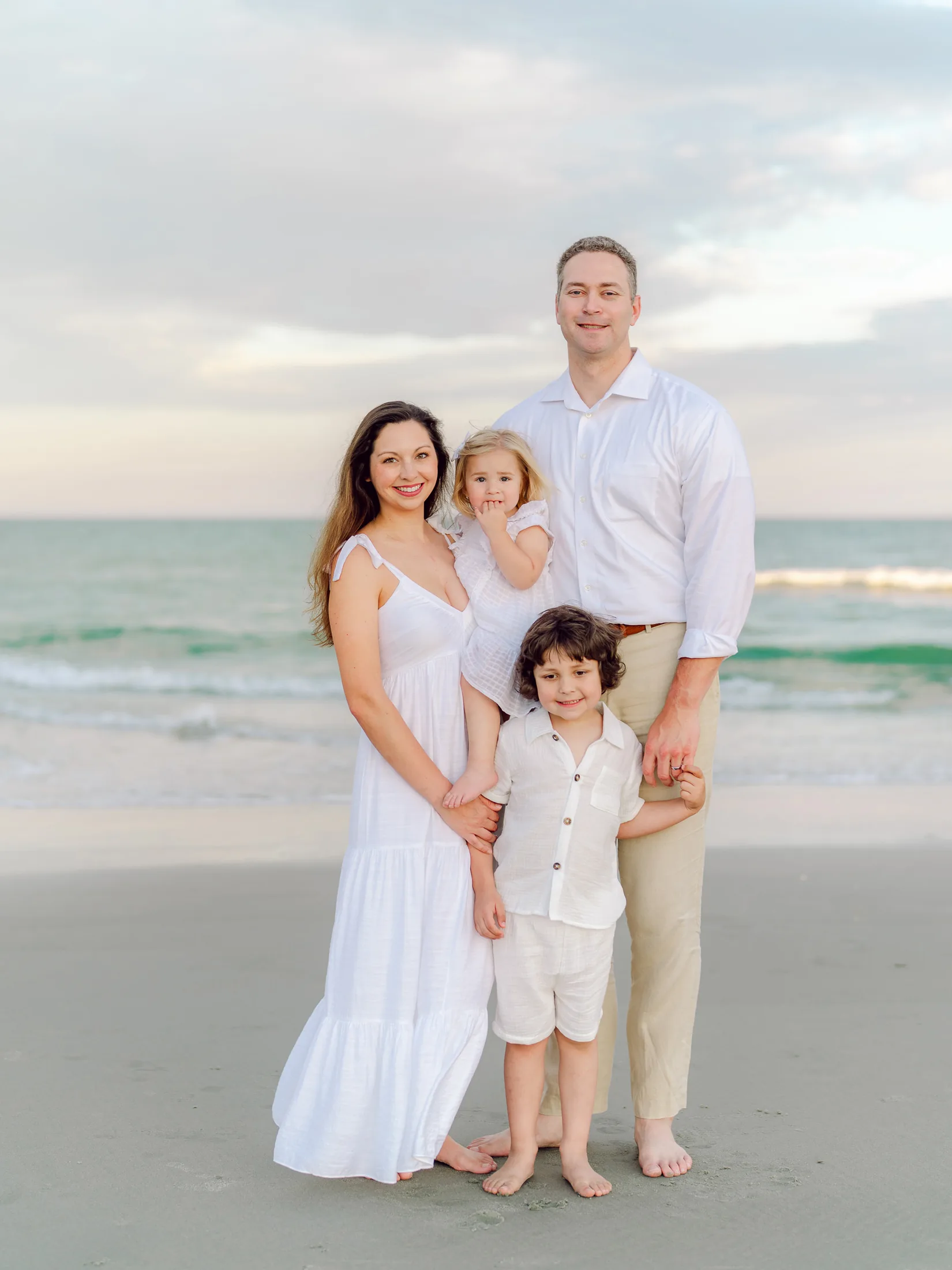 Family of four in white outfits standing on the shoreline with turquoise water behind them