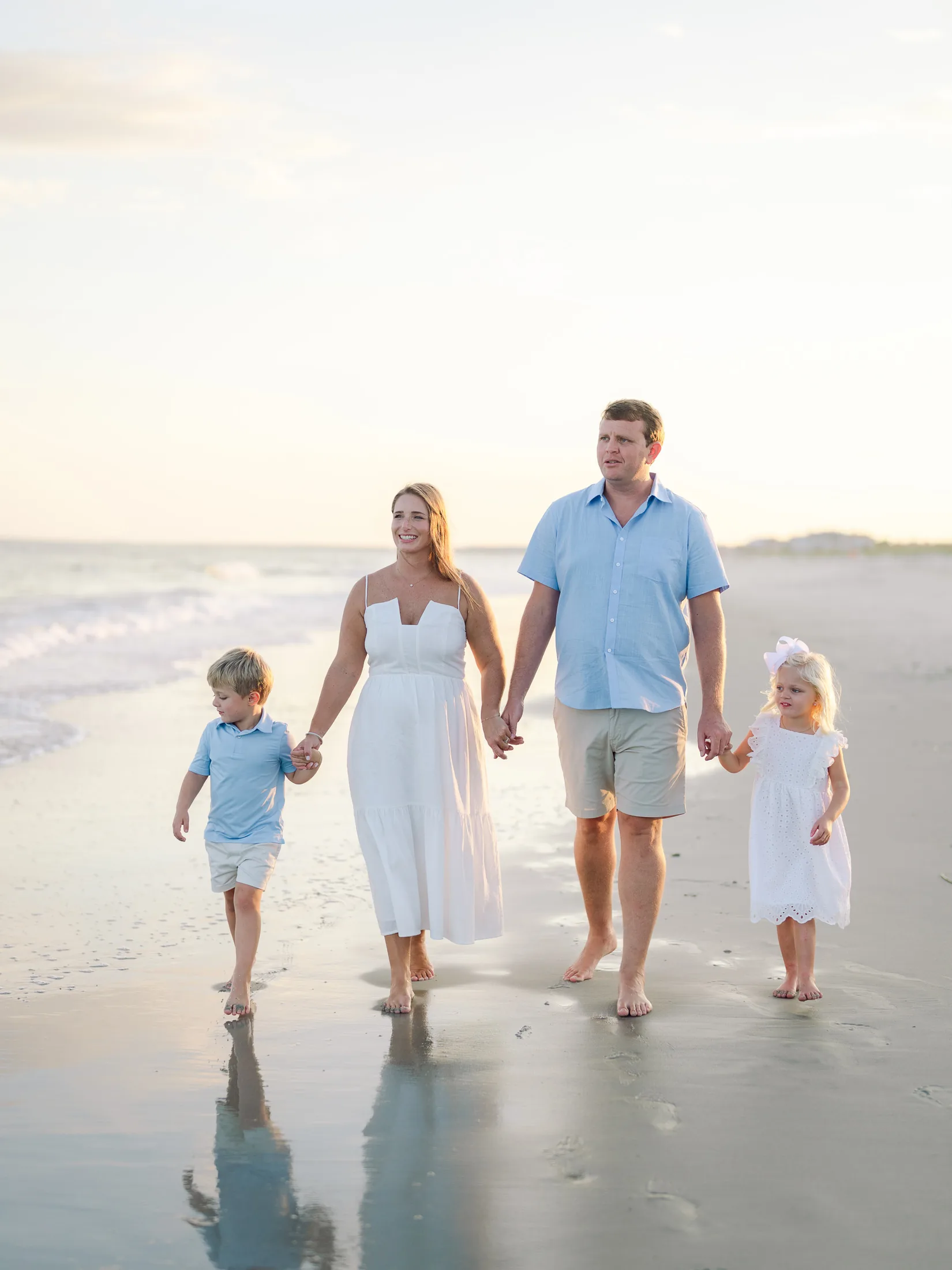 Family of four walking the shoreline at sunset with soft reflections in the wet sand
