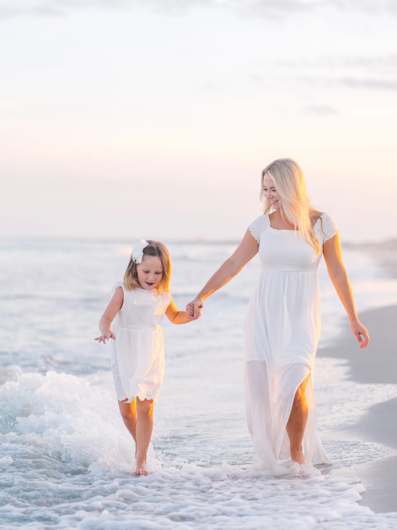 Mother and daughter holding hands and walking through the waves