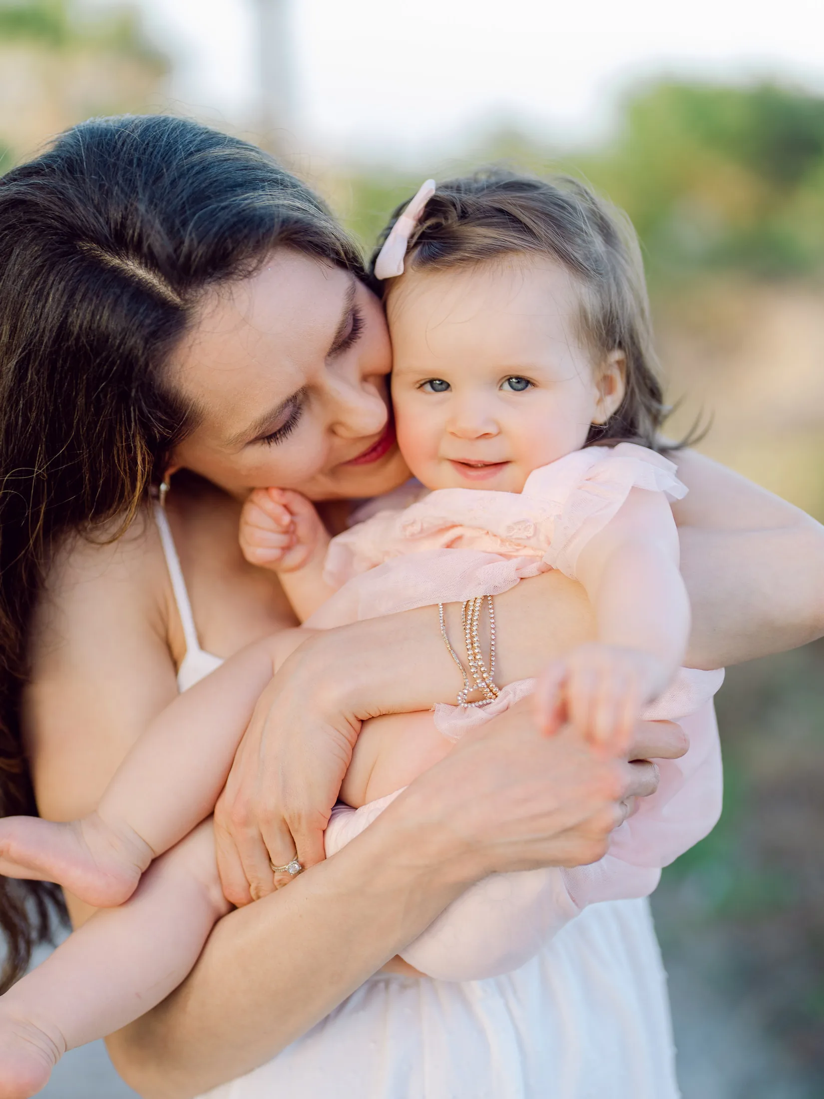Mother hugging her baby girl in a pink outfit on the beach