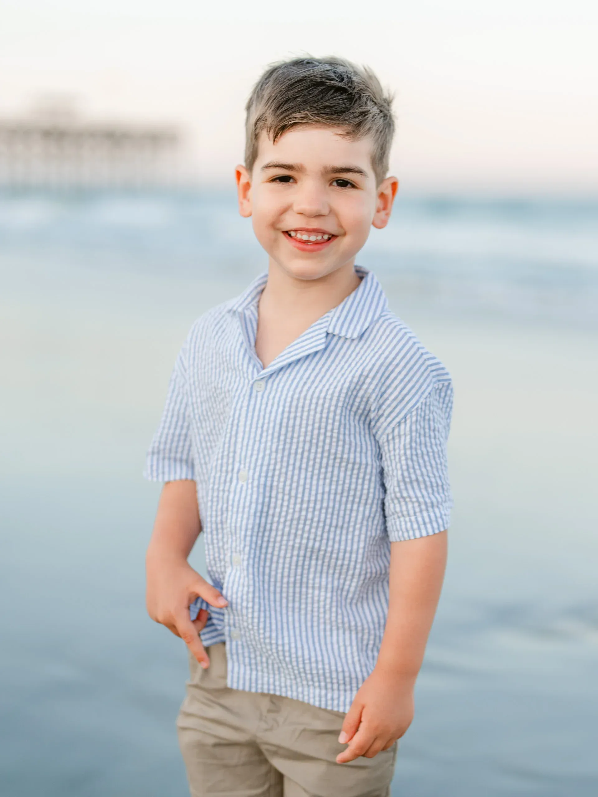 Young boy in a striped shirt at the water's edge by Pasha Belman Photography