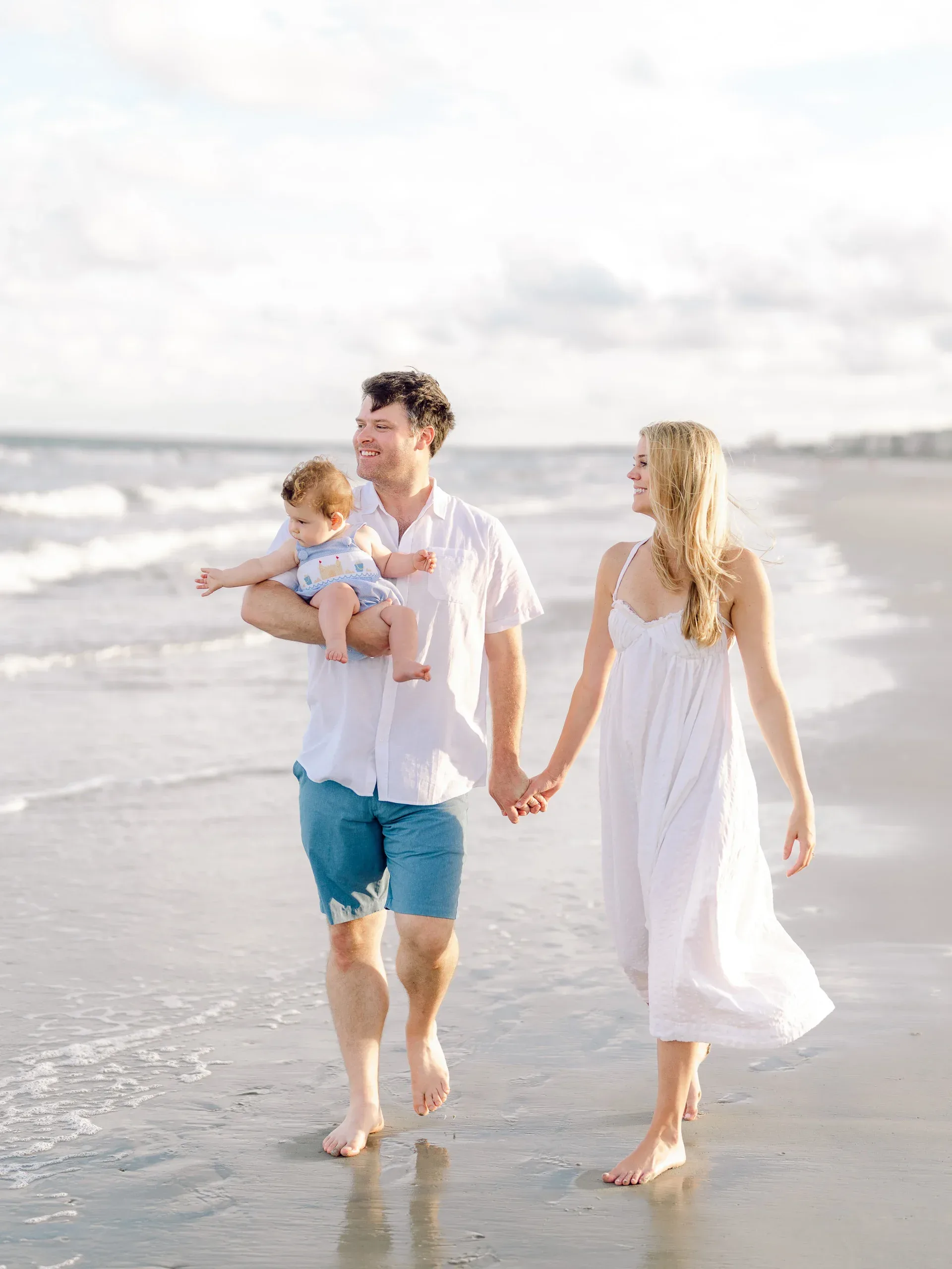Parents walking hand in hand with their children in the surf by Pasha Belman Photography