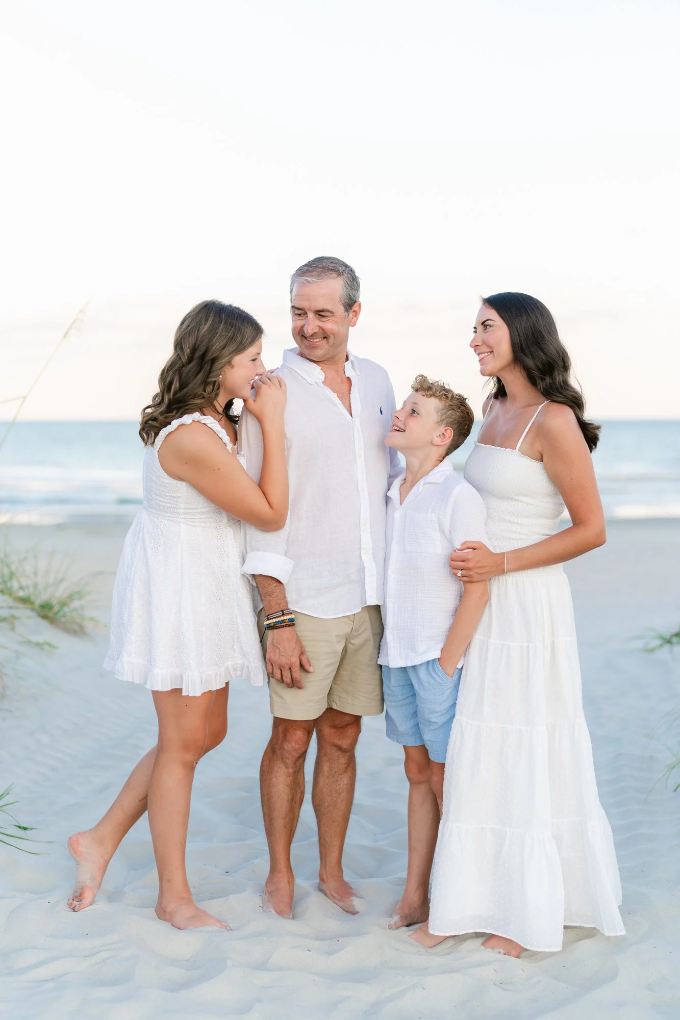 Family of four dressed in white laughing together on the beach at sunset, Myrtle Beach family photography by Pasha Belman