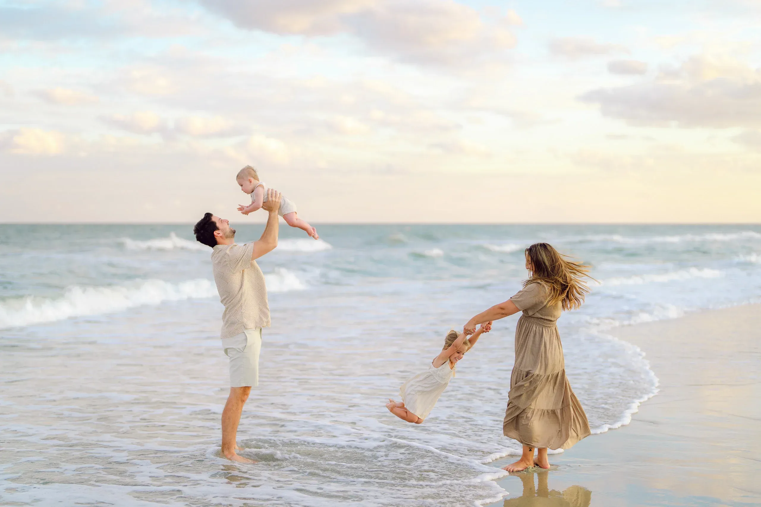 Dad lifting his son in the surf while mom and daughter play by Pasha Belman Photography