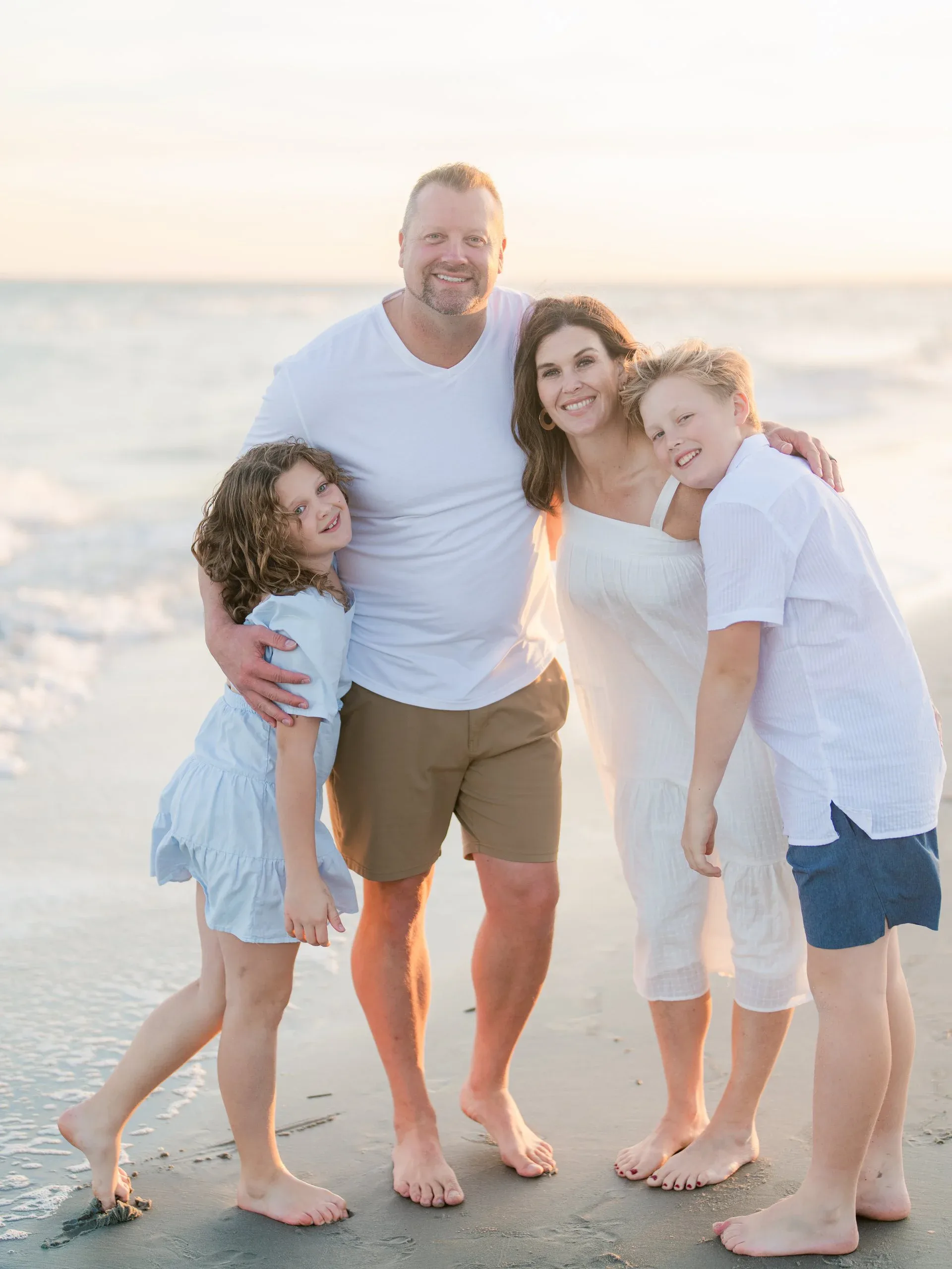 Family of four at the water's edge on the beach by Pasha Belman Photography