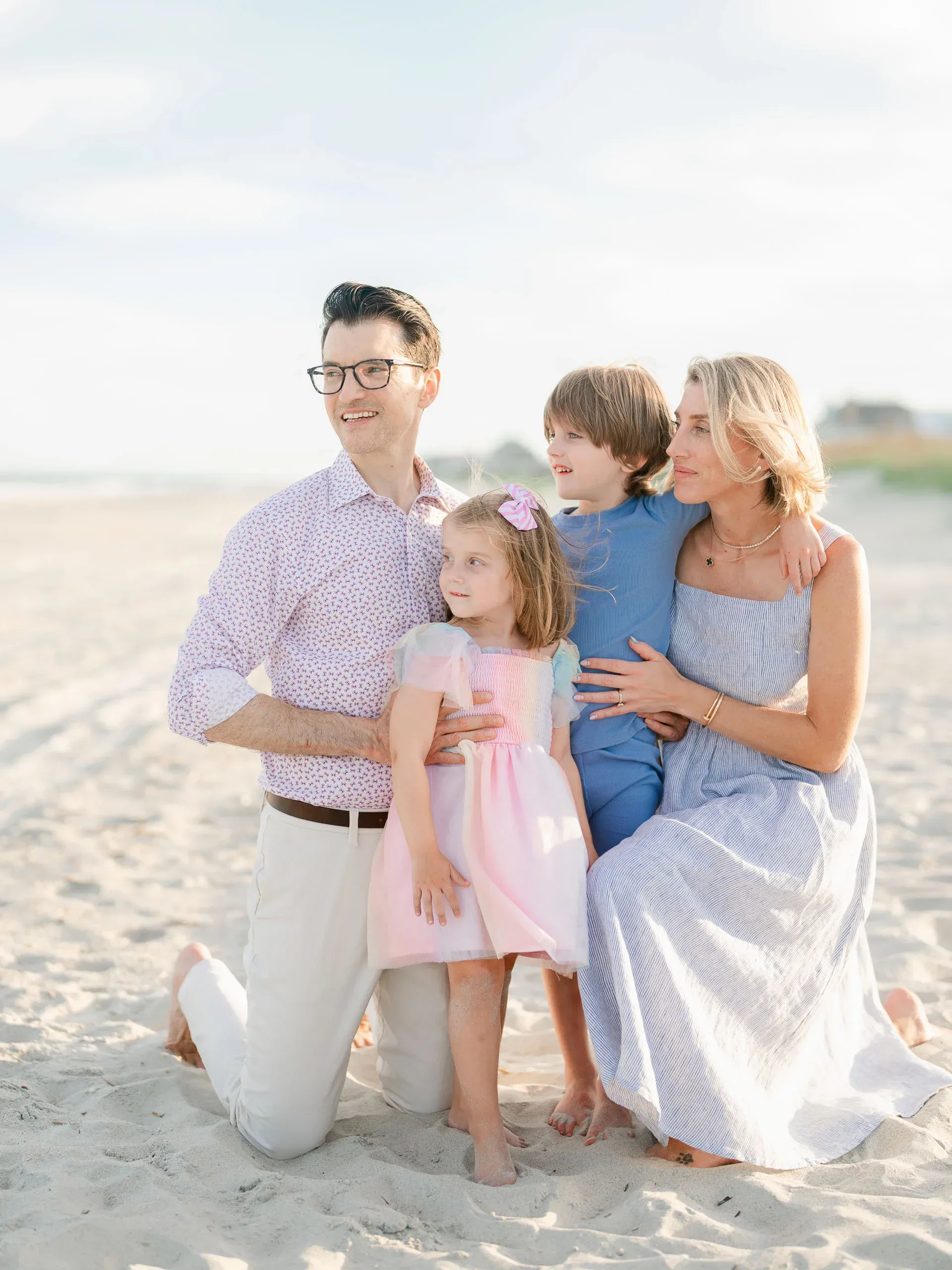 Family of four kneeling together on the sand by Pasha Belman Photography