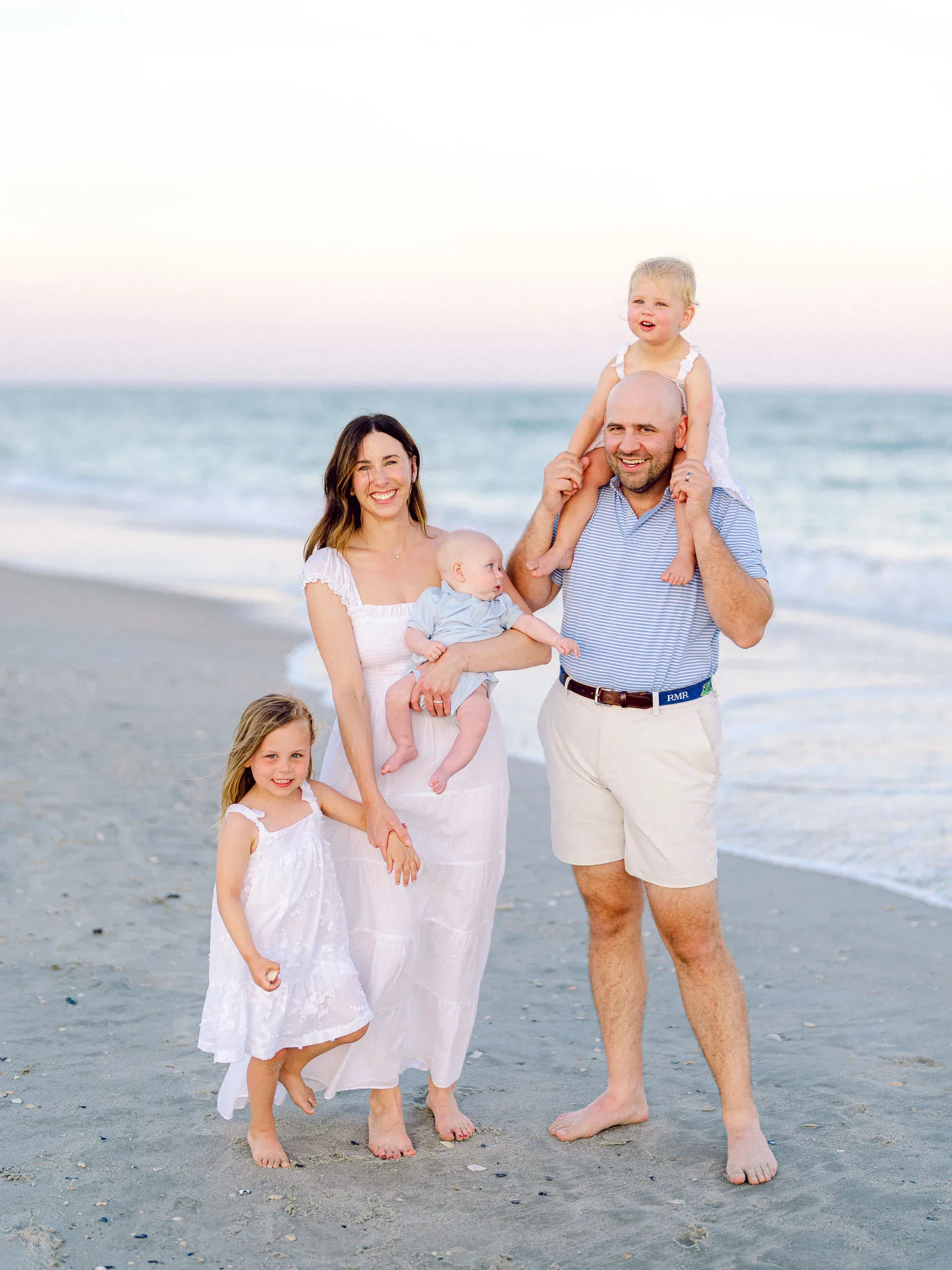 Family walking the beach with a child on dad's shoulders by Pasha Belman Photography