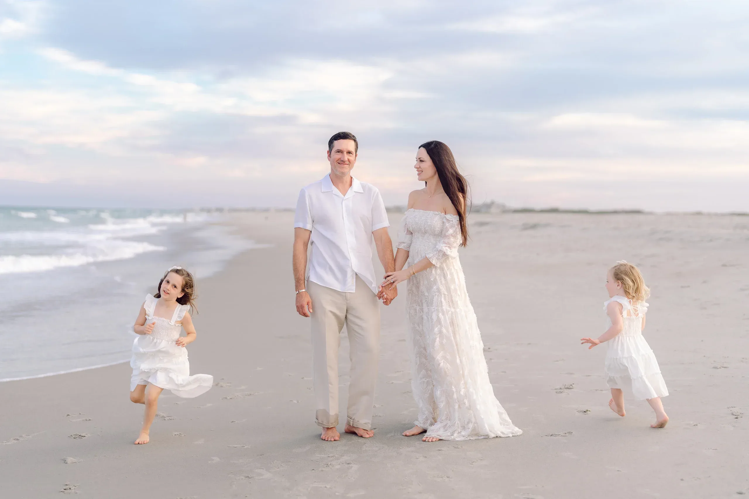 Family walking the shoreline with their young daughters by Pasha Belman Photography