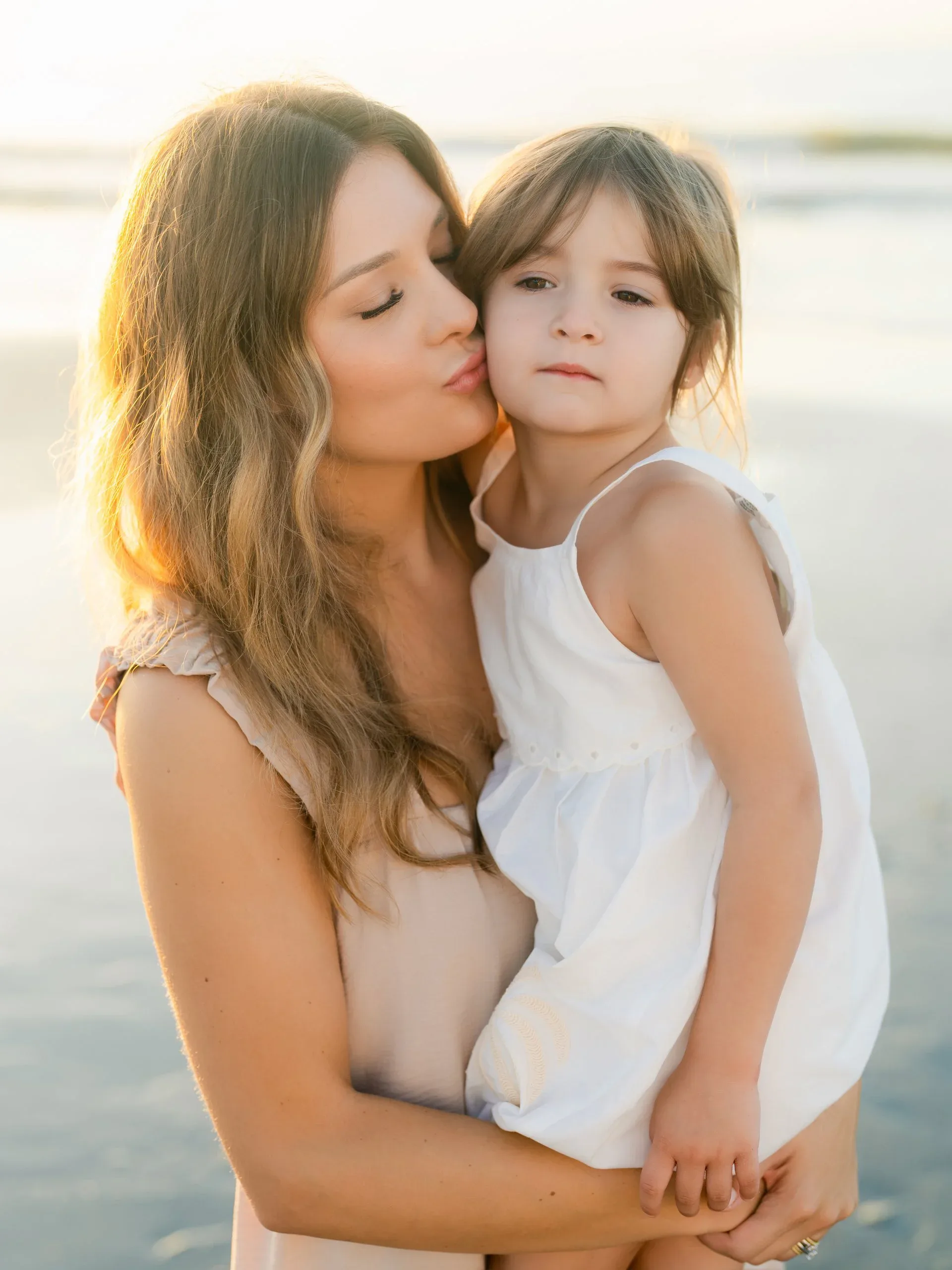 Mother kissing her daughter on the beach at sunrise by Pasha Belman Photography