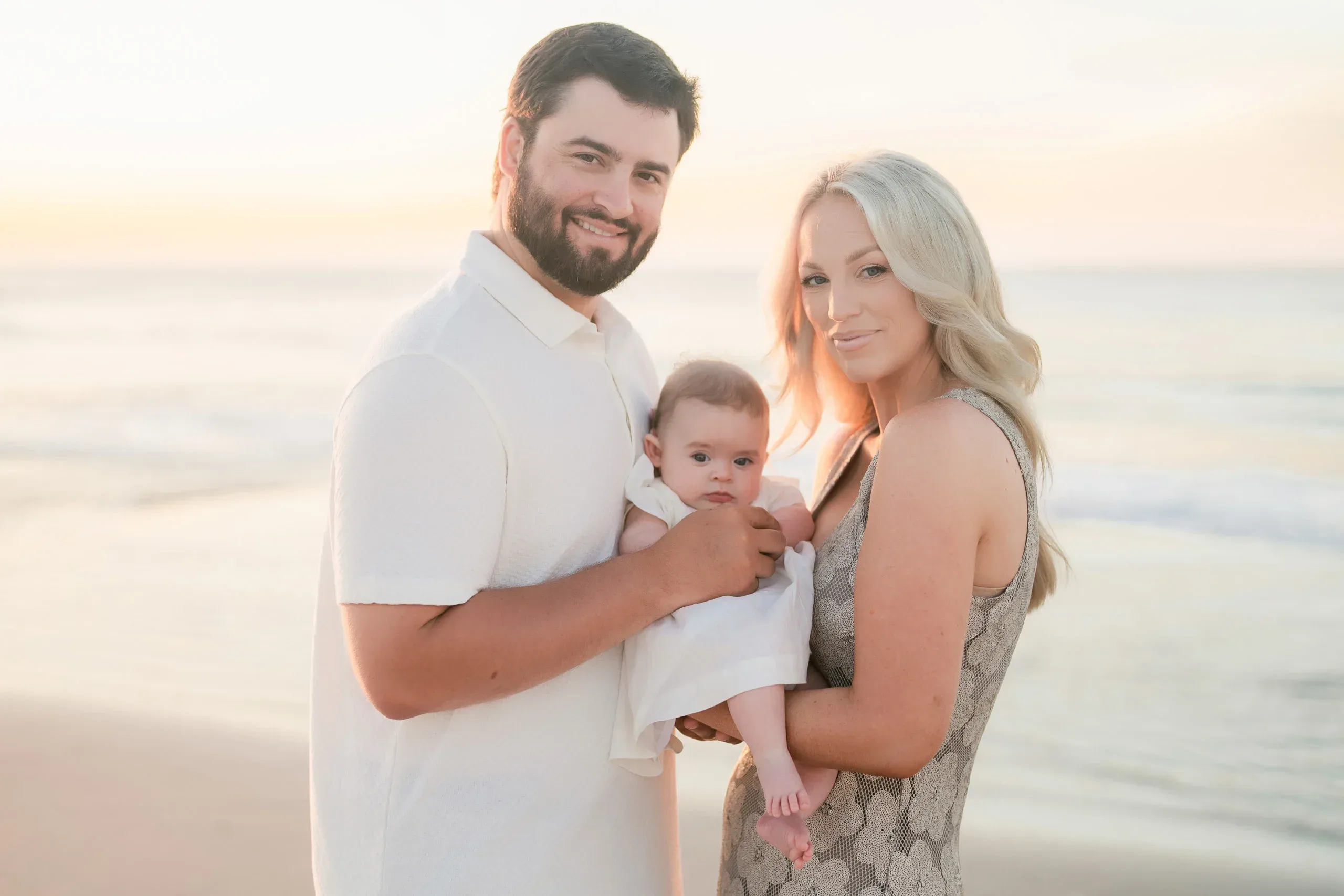 Parents holding their baby girl on the beach at sunset by Pasha Belman Photography