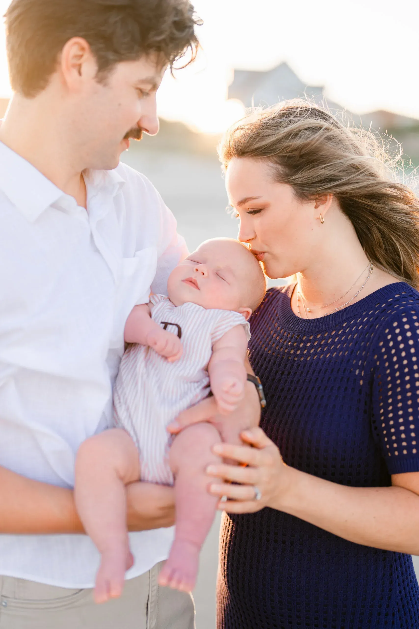 Parents kissing their newborn baby on the beach by Pasha Belman Photography