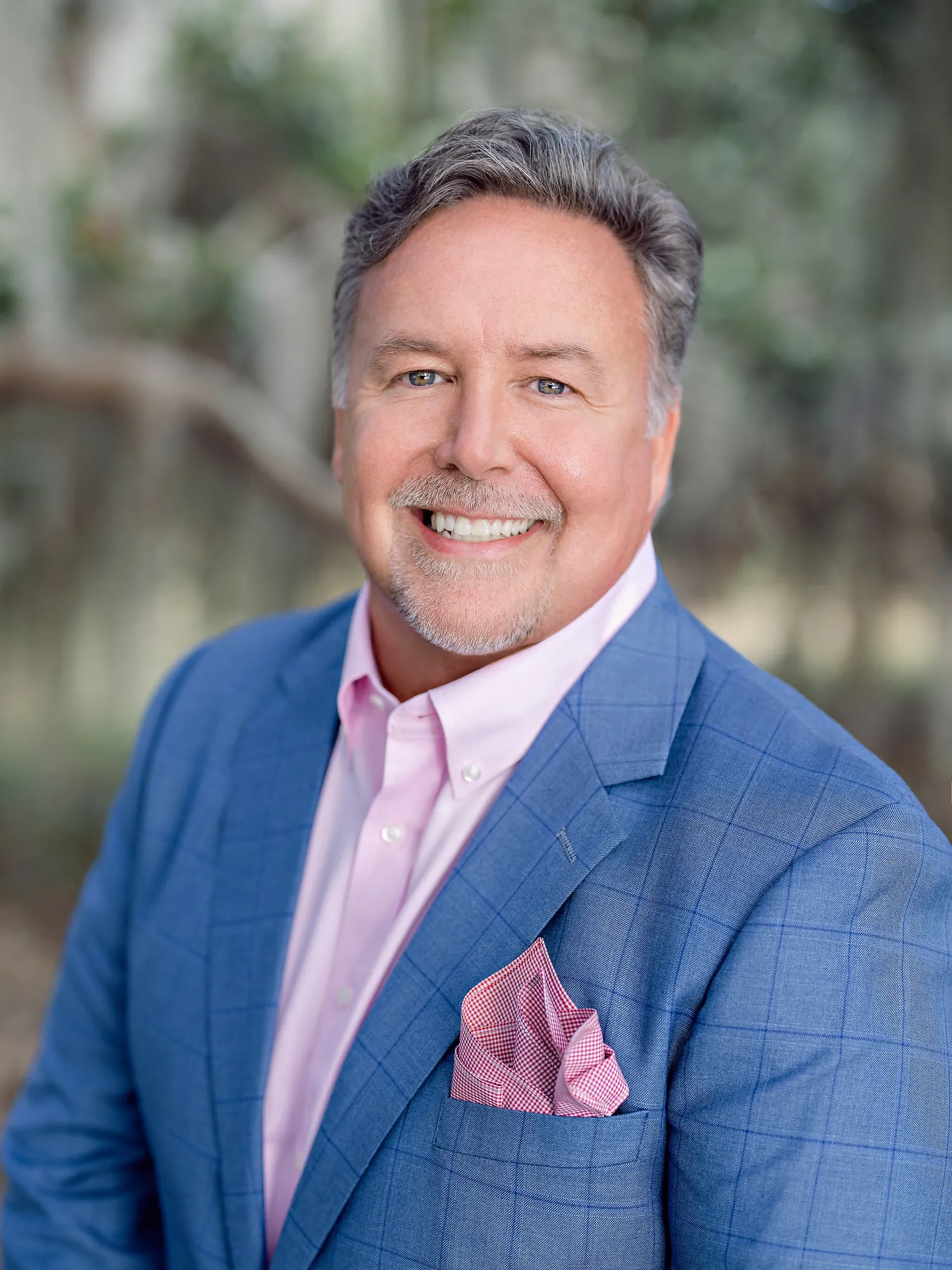 Professional headshot of a smiling man with gray hair in a blue blazer, pink shirt and pink pocket square by Myrtle Beach headshot photographer Pasha Belman
