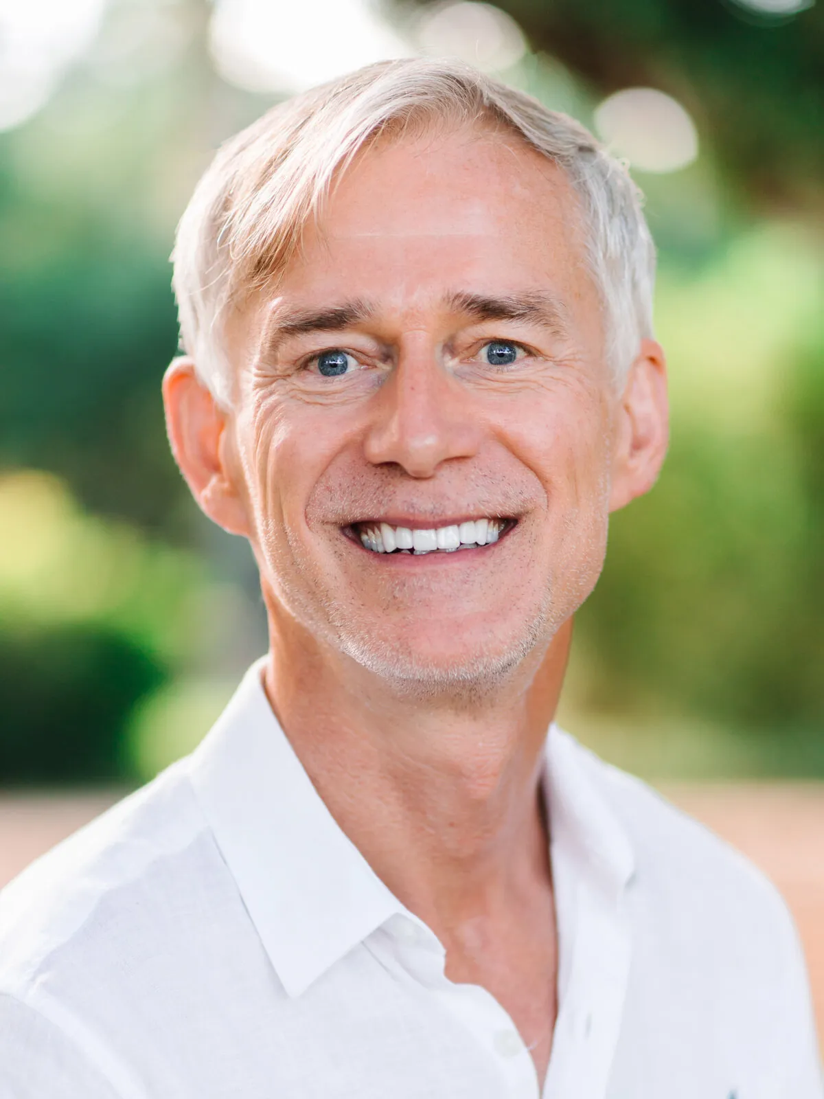 Professional headshot of a smiling man with silver-white hair in a white linen shirt, outdoors by Myrtle Beach headshot photographer Pasha Belman