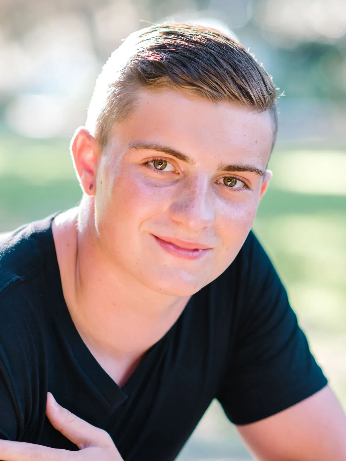 Professional headshot of a teenage boy in a black v-neck t-shirt with his arms crossed, outdoors by Myrtle Beach headshot photographer Pasha Belman