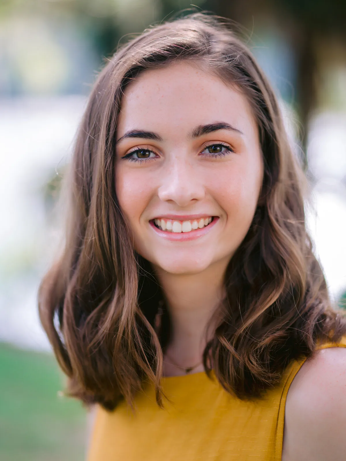 Professional headshot of a smiling teenage girl with mid-length brown hair in a mustard top, outdoors by Myrtle Beach headshot photographer Pasha Belman