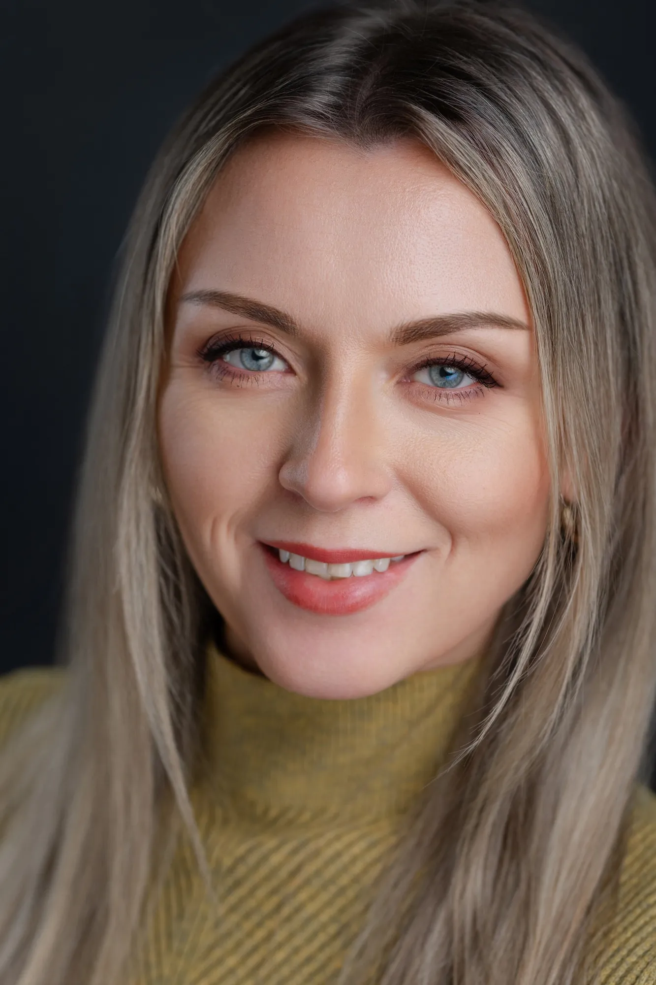Professional headshot of a woman with long hair in a mustard turtleneck against a dark studio background by Myrtle Beach headshot photographer Pasha Belman