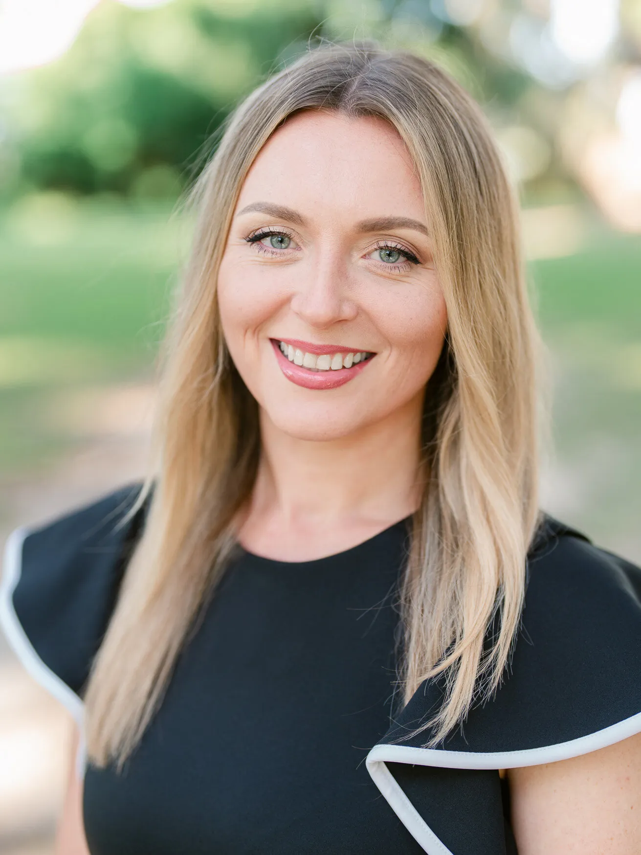 Professional headshot of a smiling woman with long blonde hair in a black top with white trim, outdoors by Myrtle Beach headshot photographer Pasha Belman