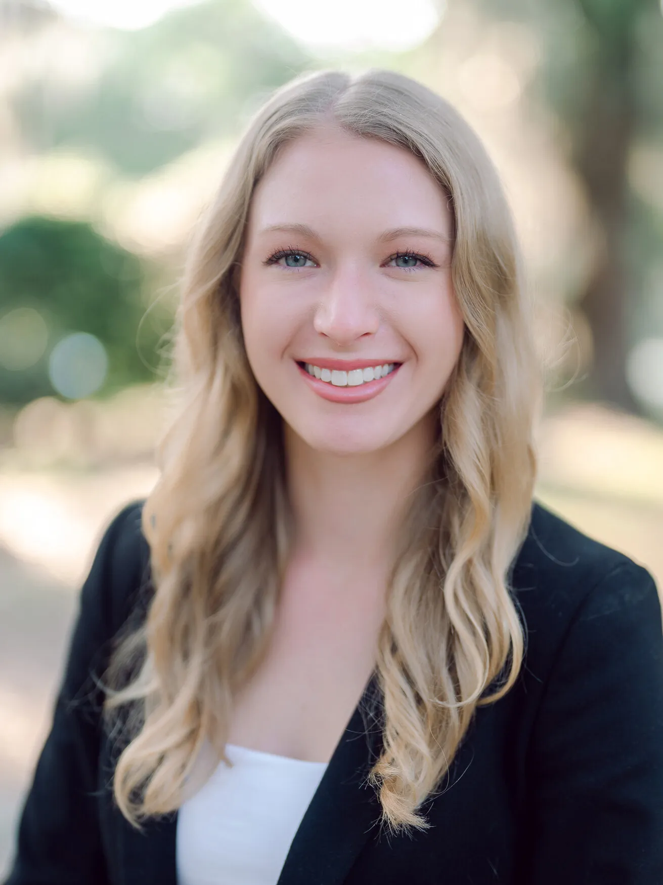 Professional headshot of a woman with long blonde hair in a dark blazer over a white top, outdoors by Myrtle Beach headshot photographer Pasha Belman